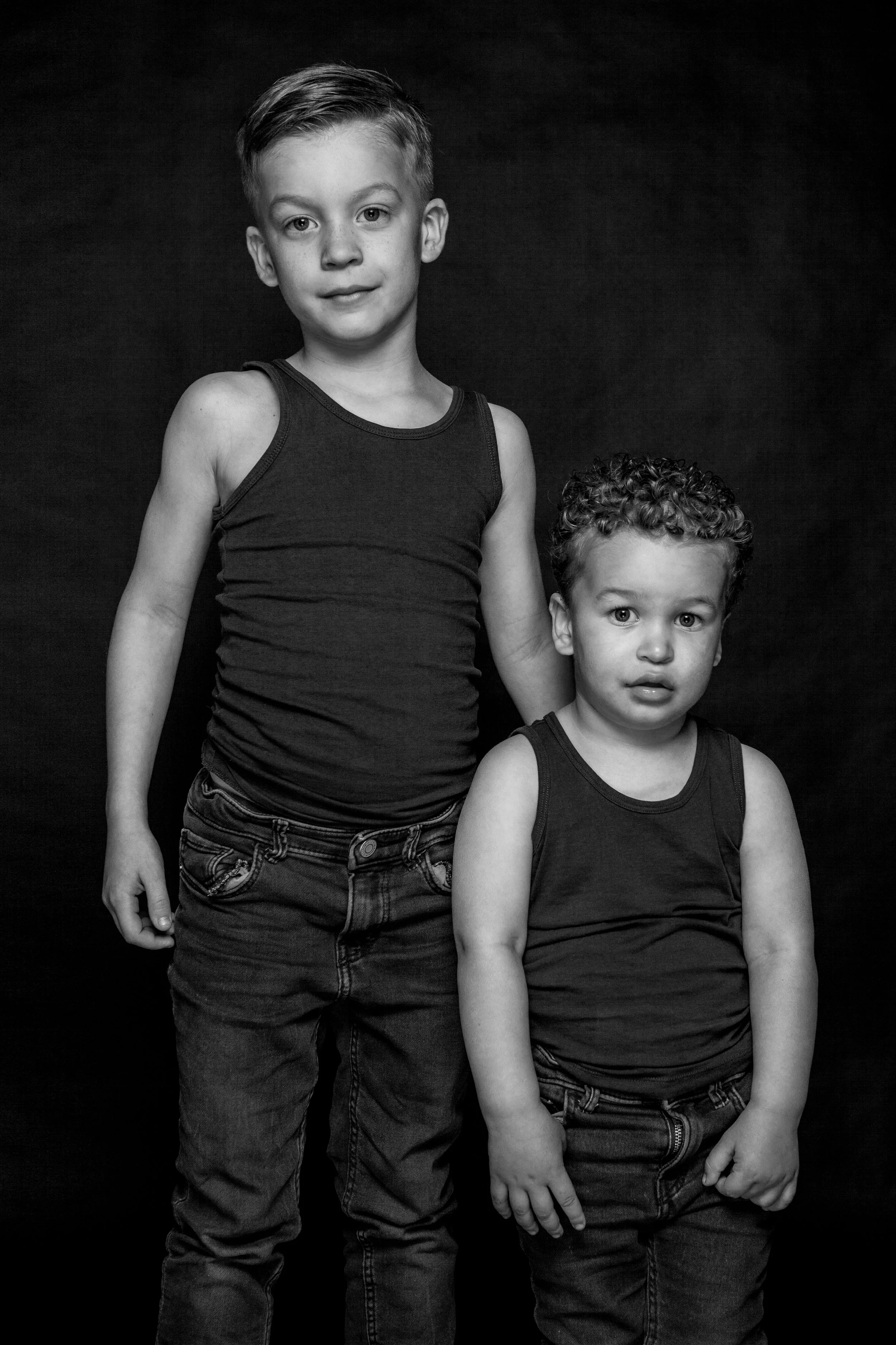 twee jonge jongens in zwarte shirts en jeans poseert voor een zwarte achtergrond, zwart-wit foto