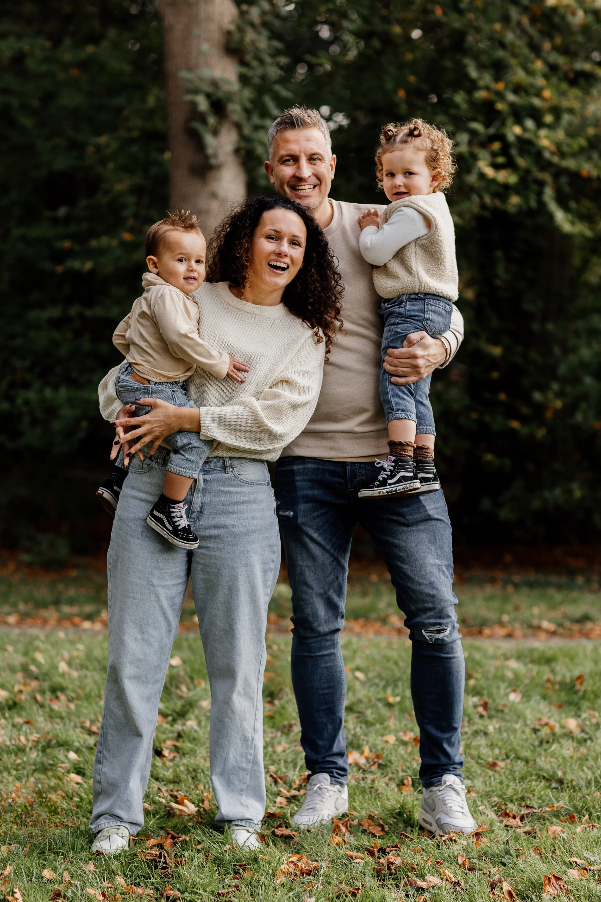 Een vrolijk gezinnetje met twee jonge kinderen in een park met herfstbladeren.
