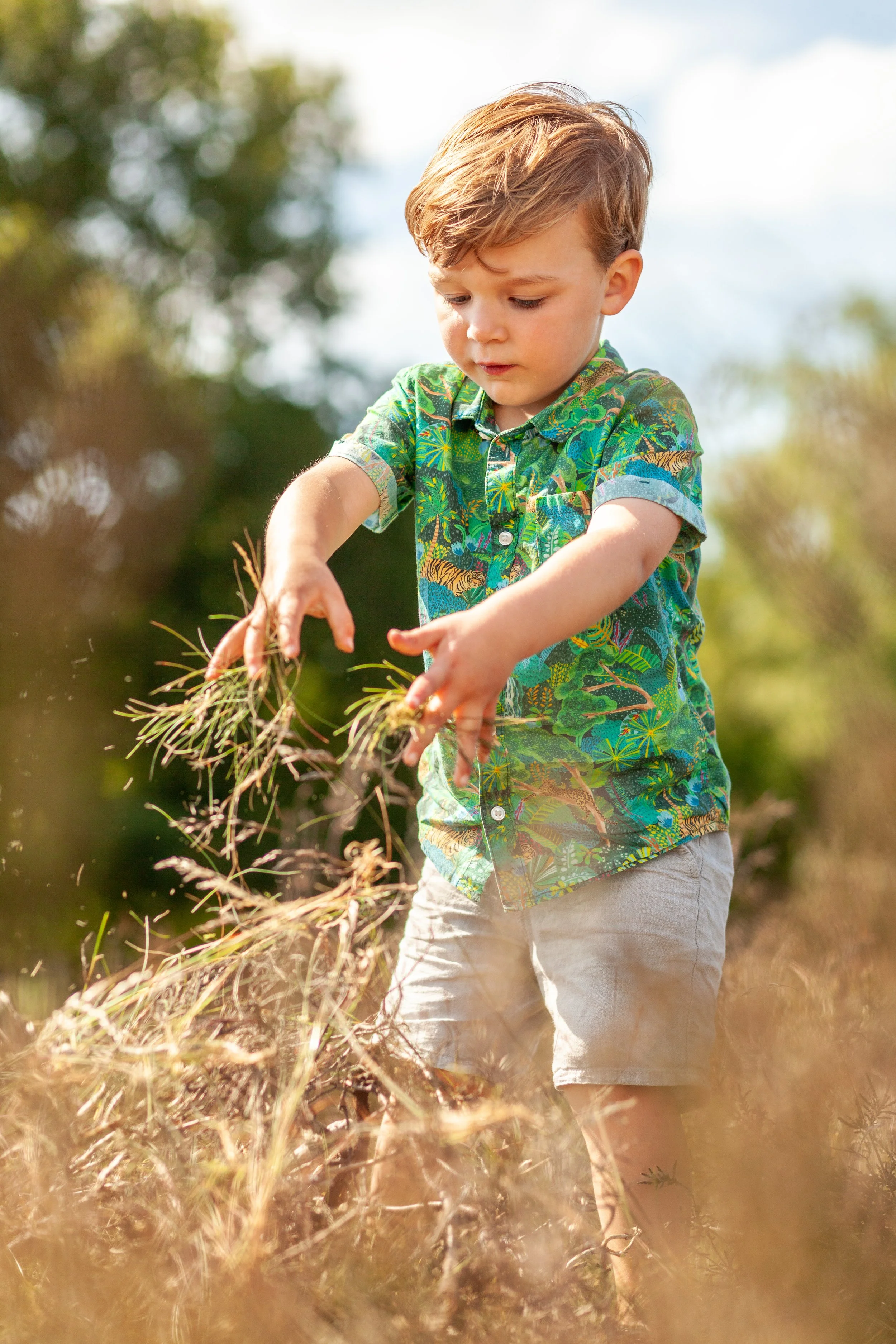 Een jonge jongen met een kleurrijk shirt draait zich om terwijl hij in een veld met droge grassprietjes aan het spelen is.