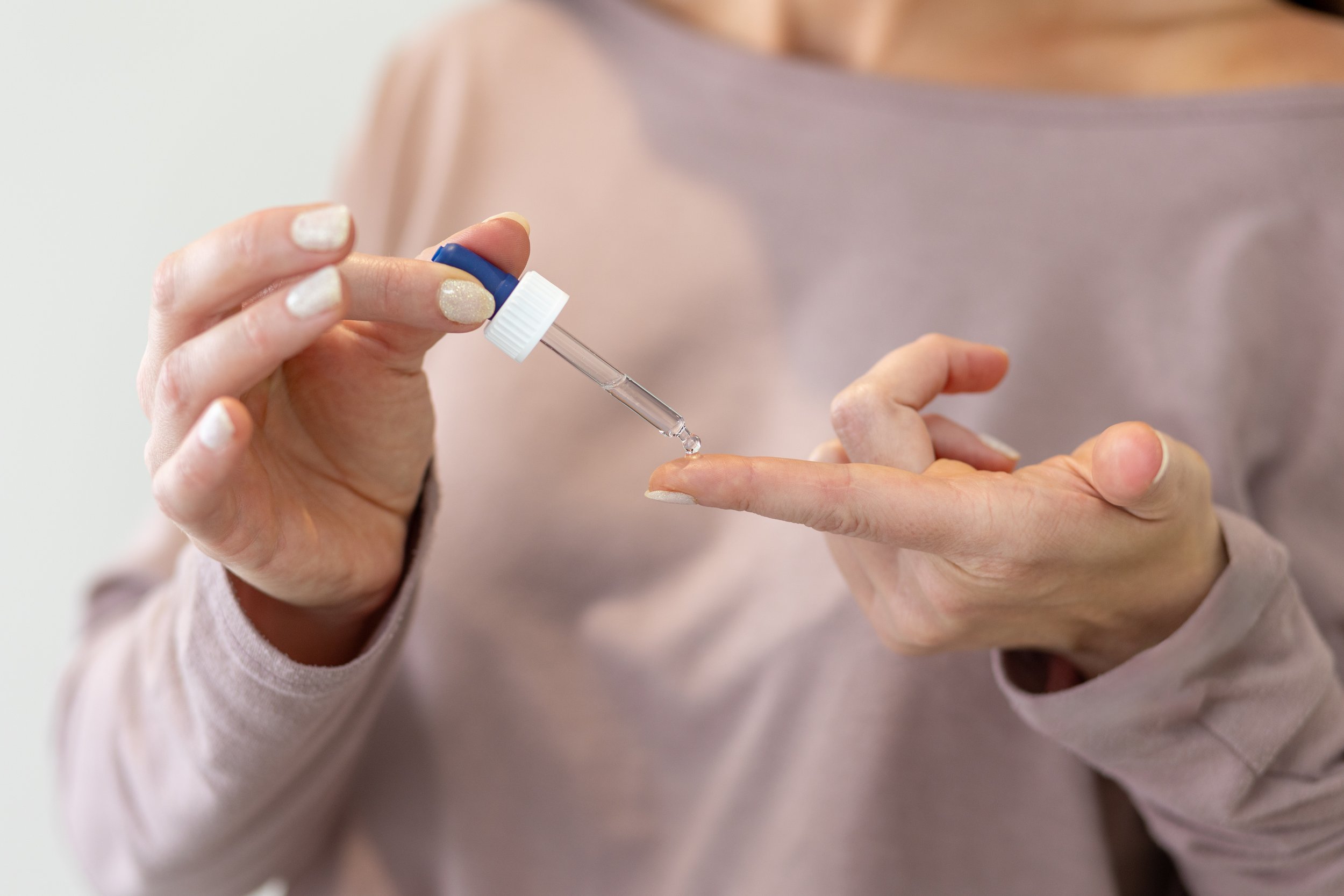 Persoon die een vloeistof met een pipet op haar vinger aanbrengt.