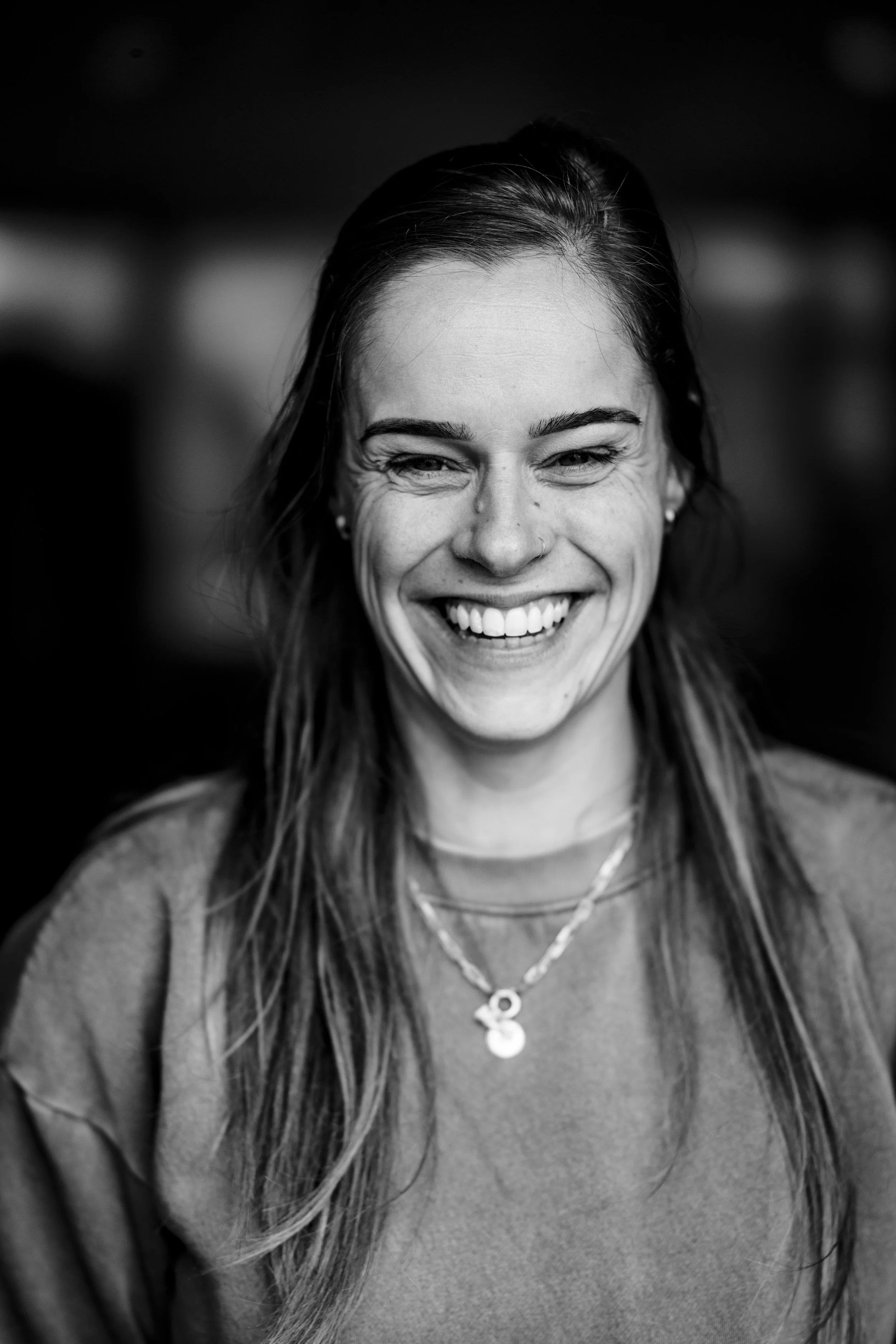 Zwart-wit foto van een lachende vrouw met lang haar, sieraden en een trui.