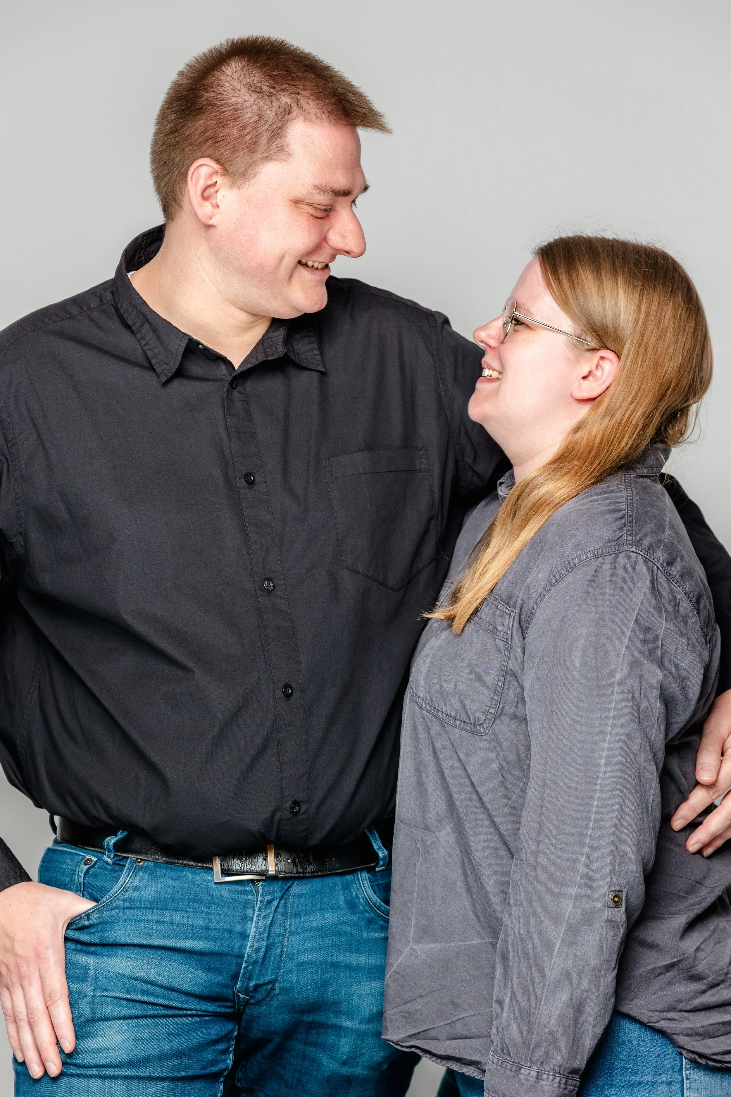 Twee mensen lachen en kijken naar elkaar, met armen om elkaar heen, tegen een lichte achtergrond.