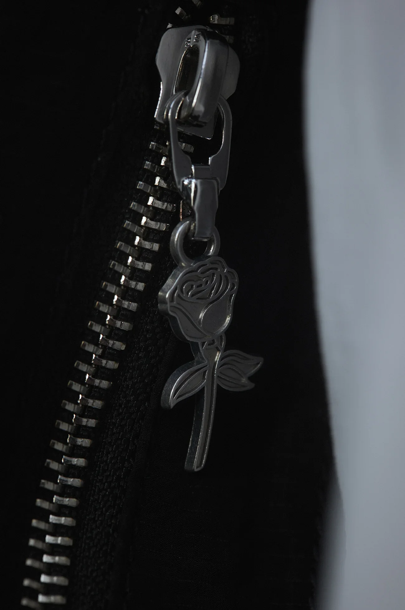 Sluiting van een zwarte tas met een zilveren rits en een metalen rose-penning in de vorm van een roos.