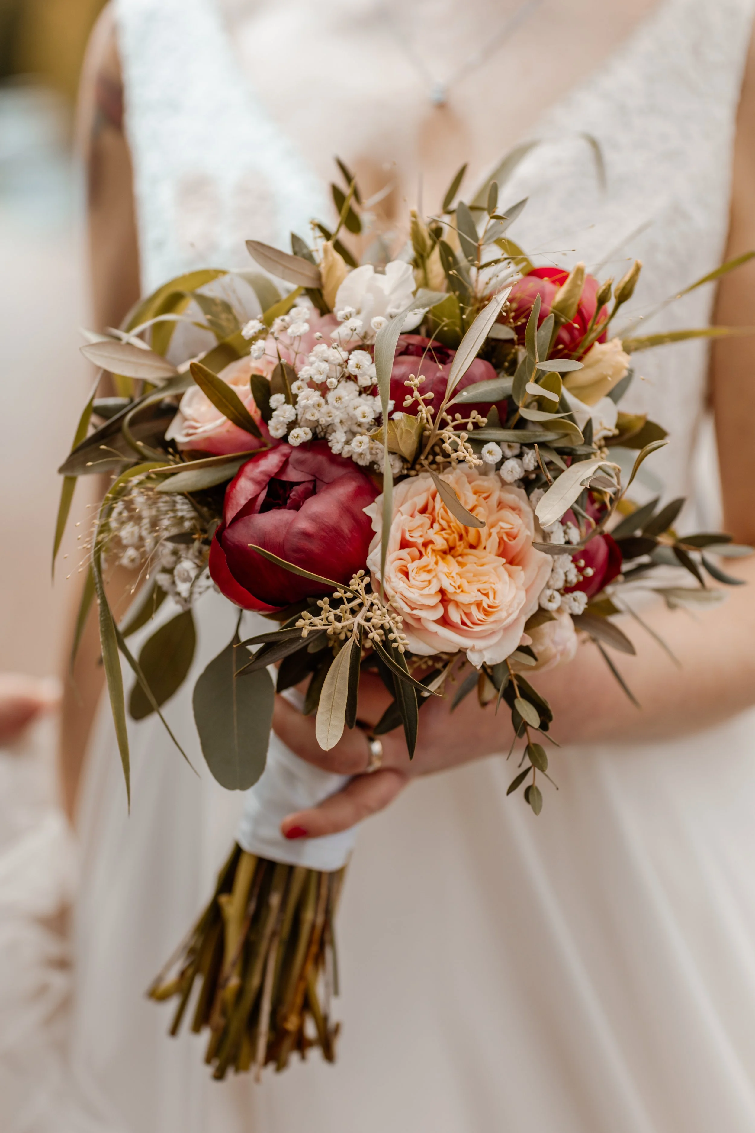 Close-up van een bruidsboeket met bloemen en groene bladeren, vastgehouden door een vrouwelijke bruid bij haar huwelijk.