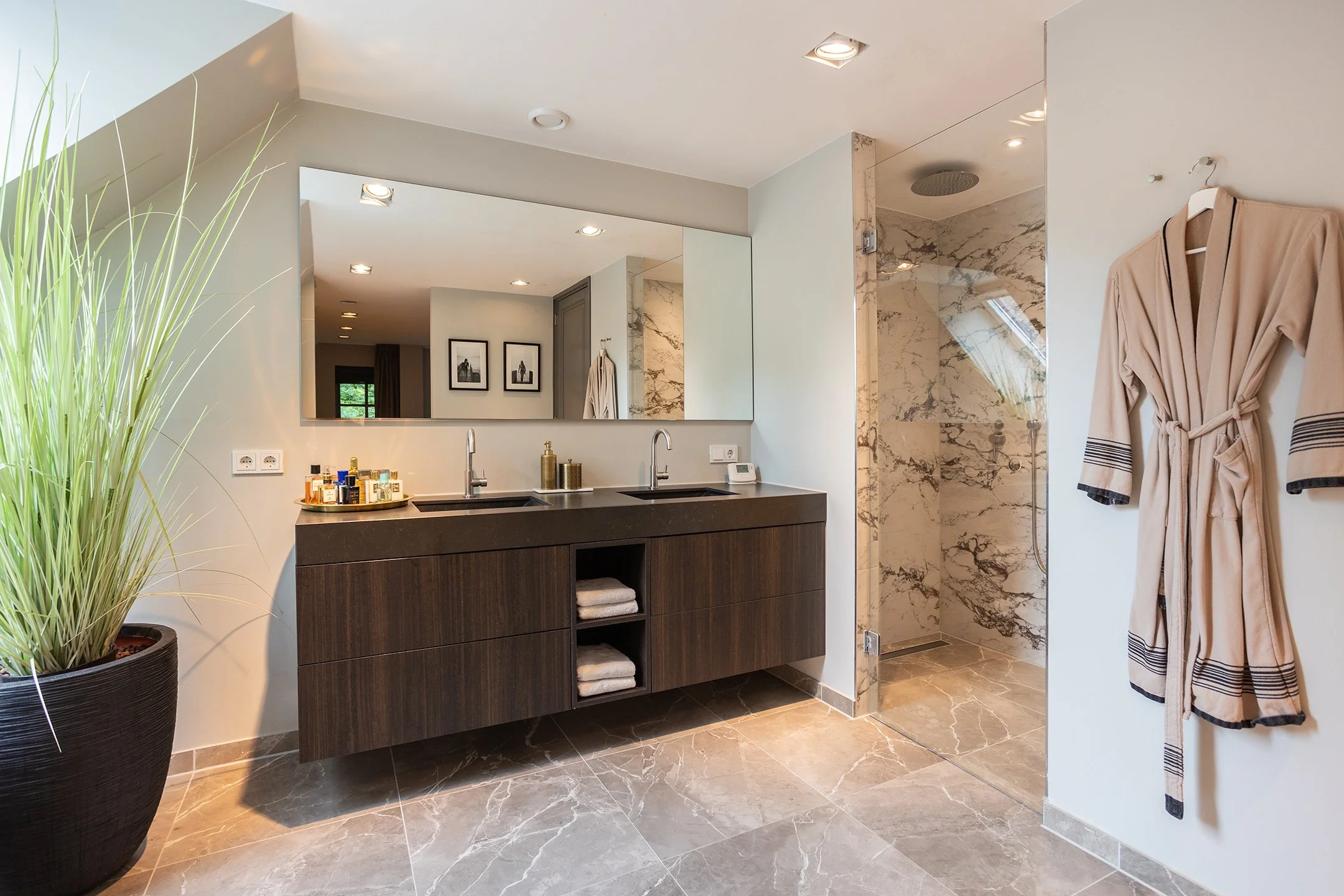 Moderne badkamer met dubbele wastafel, spiegel, ligbad, inloopdouche en badjas aan de muur.