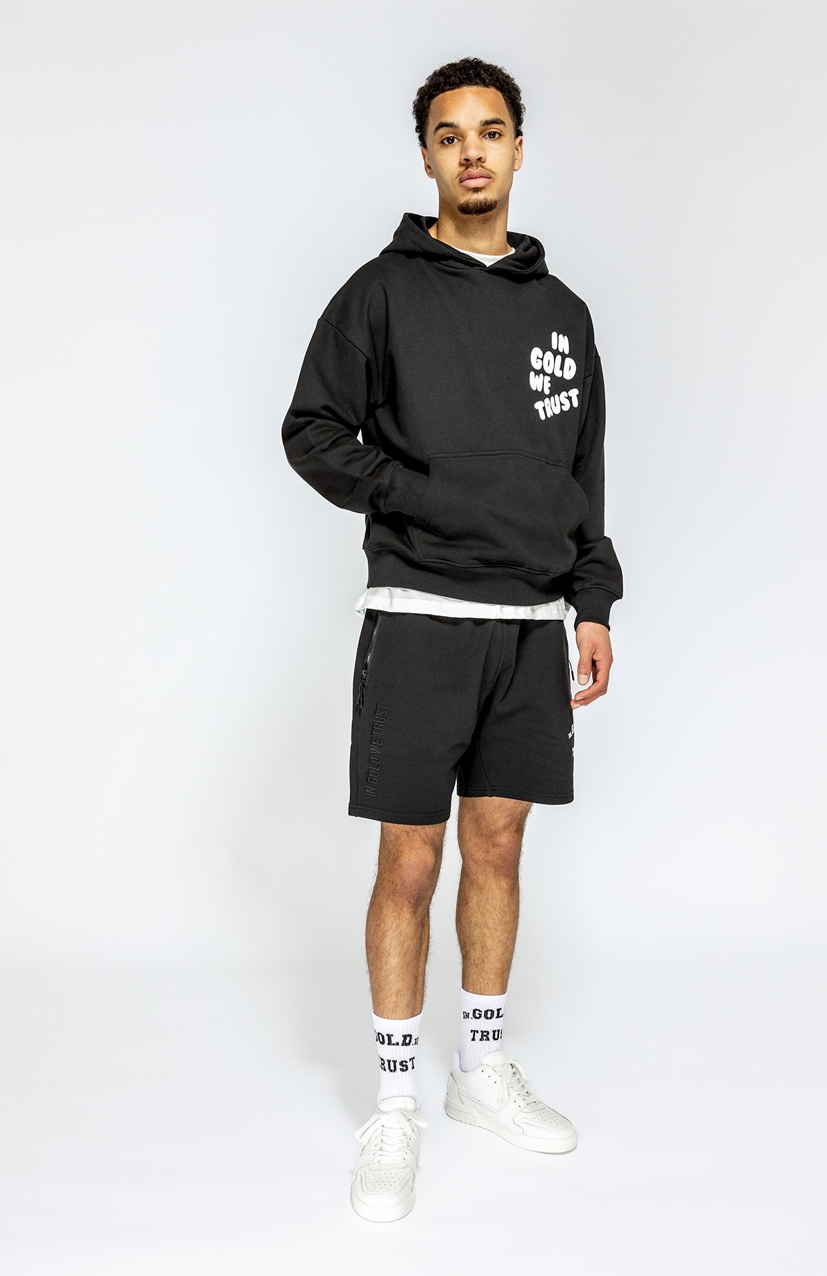 Jongen in zwart hoodie en short op witte achtergrond.