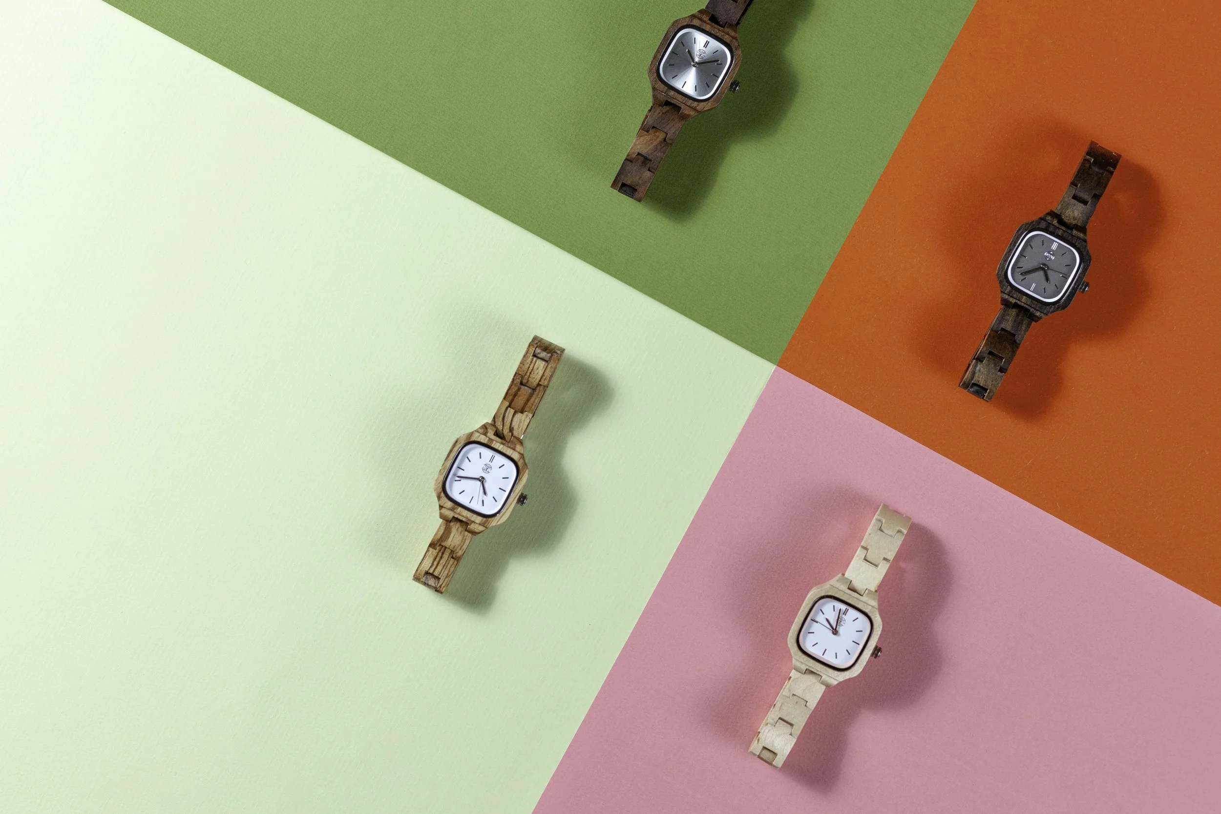 Vijf houten horloges op gekleurde achtergronddelen in groen, oranje, roze en lichtgroen.