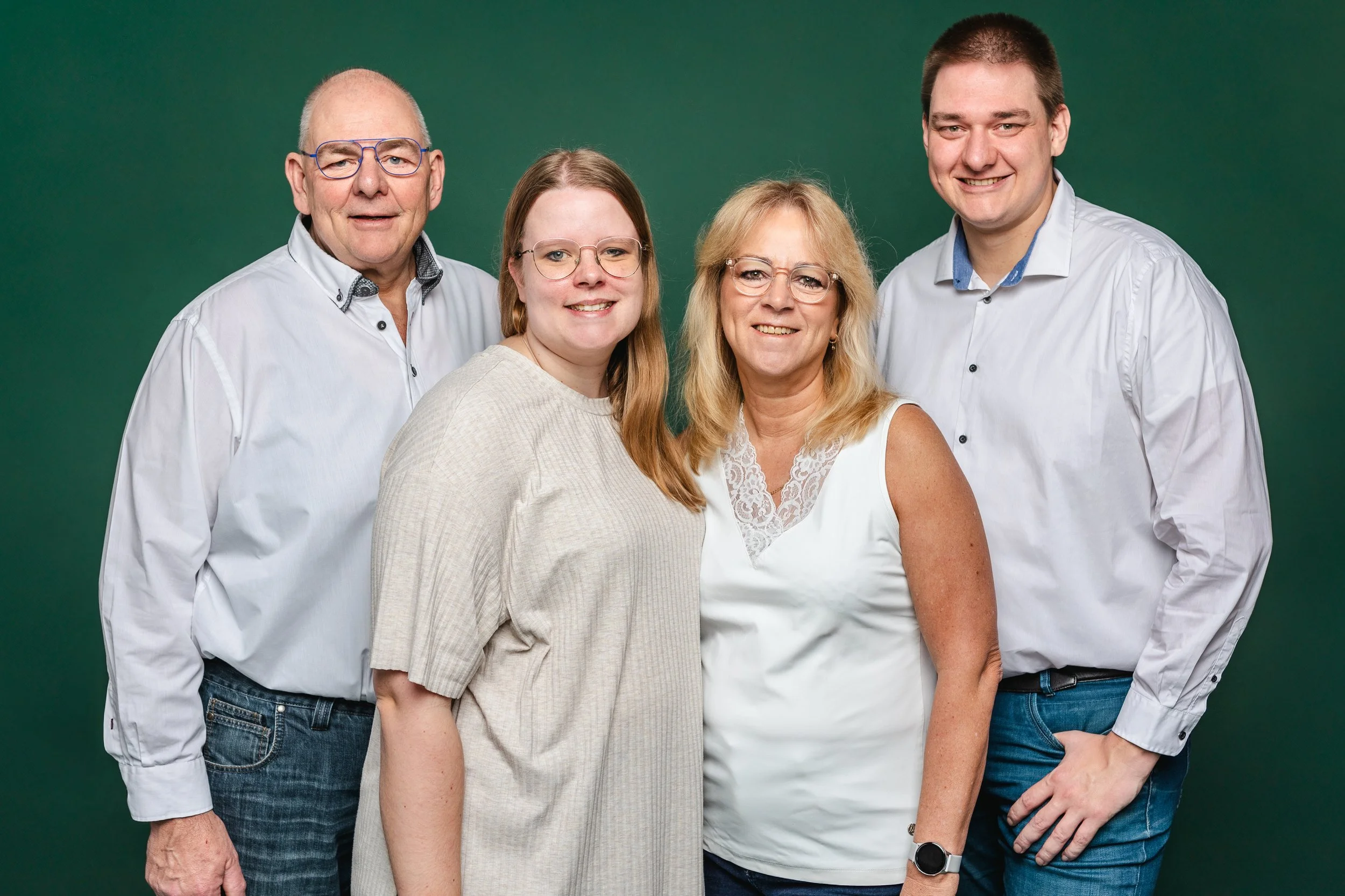 Groep van vijf mensen poseert samen tegen een groene achtergrond, vier volwassenen en één tiener, allemaal glimlachend.