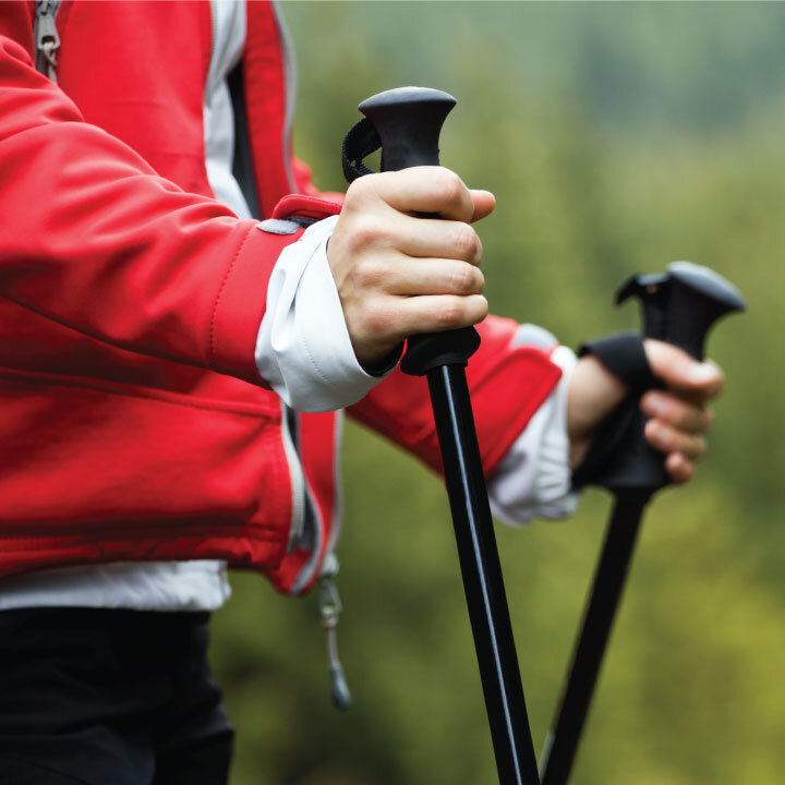  Close-up photo of a middle aged women carrying Nordic poles to help her walk through the woods. 