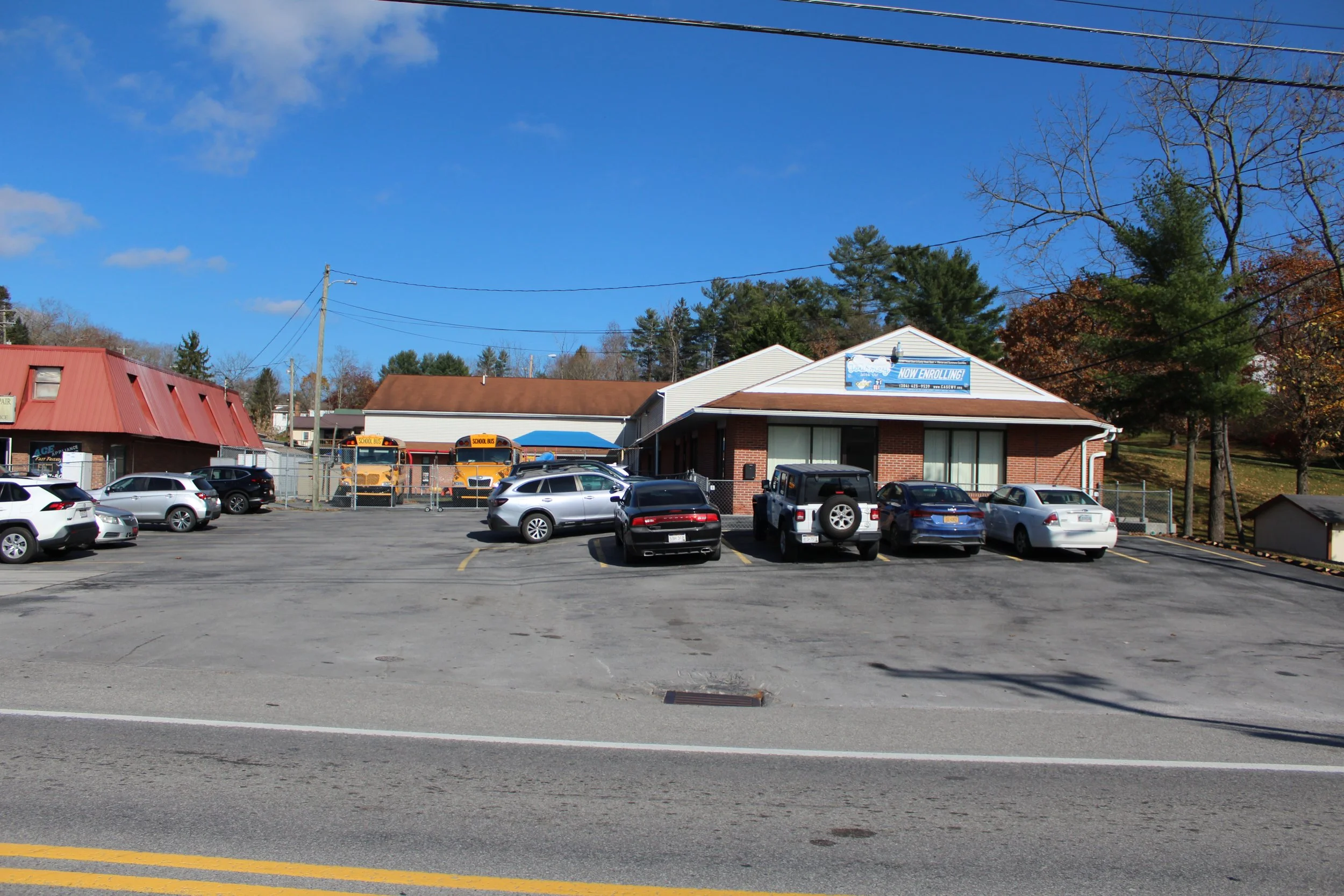 Parking lot in front of a building with school bus stops, surrounded by trees and a blue sky.
