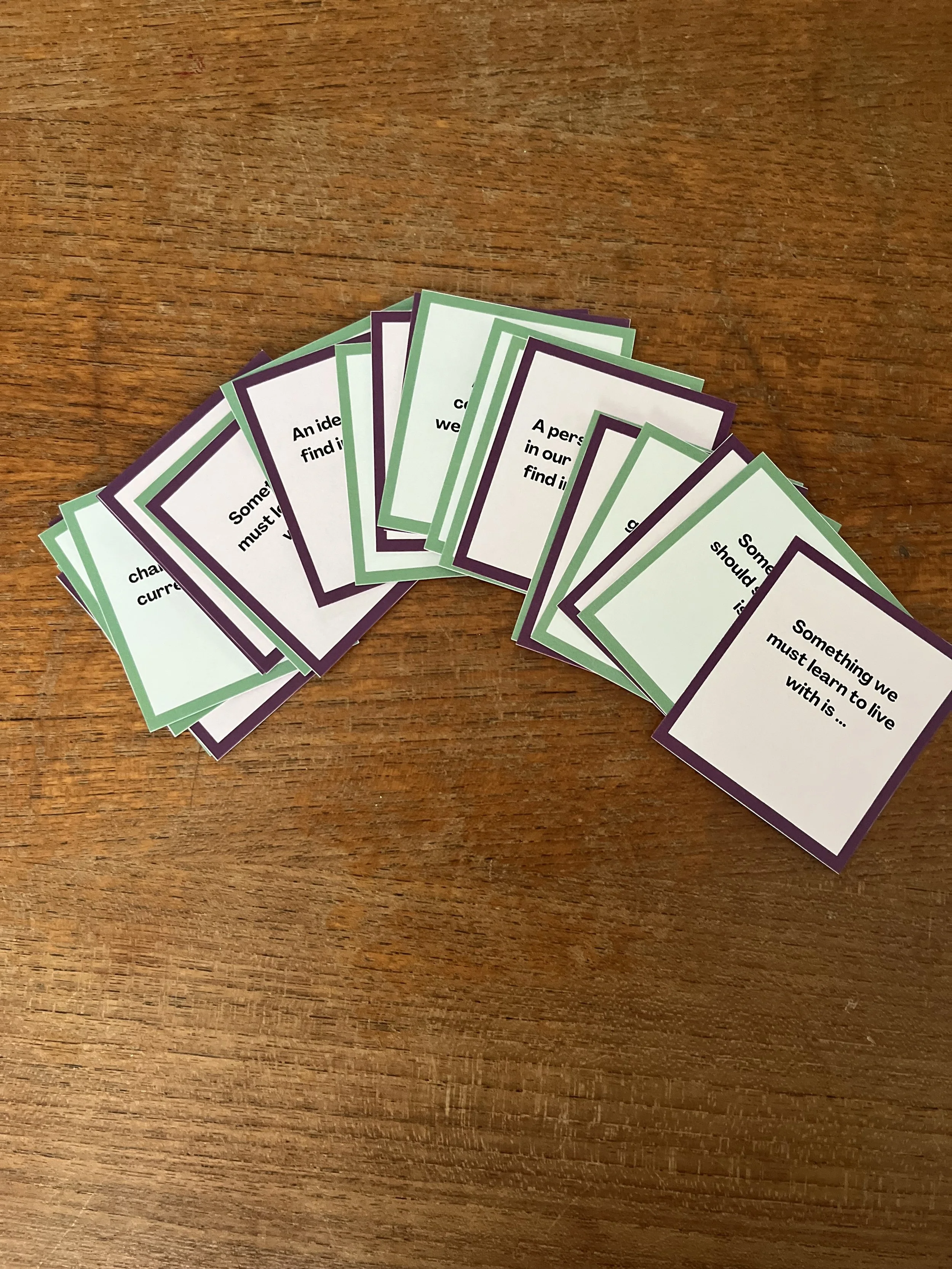 Stack of small cards with green and purple borders and inspirational quotes on a wooden surface.