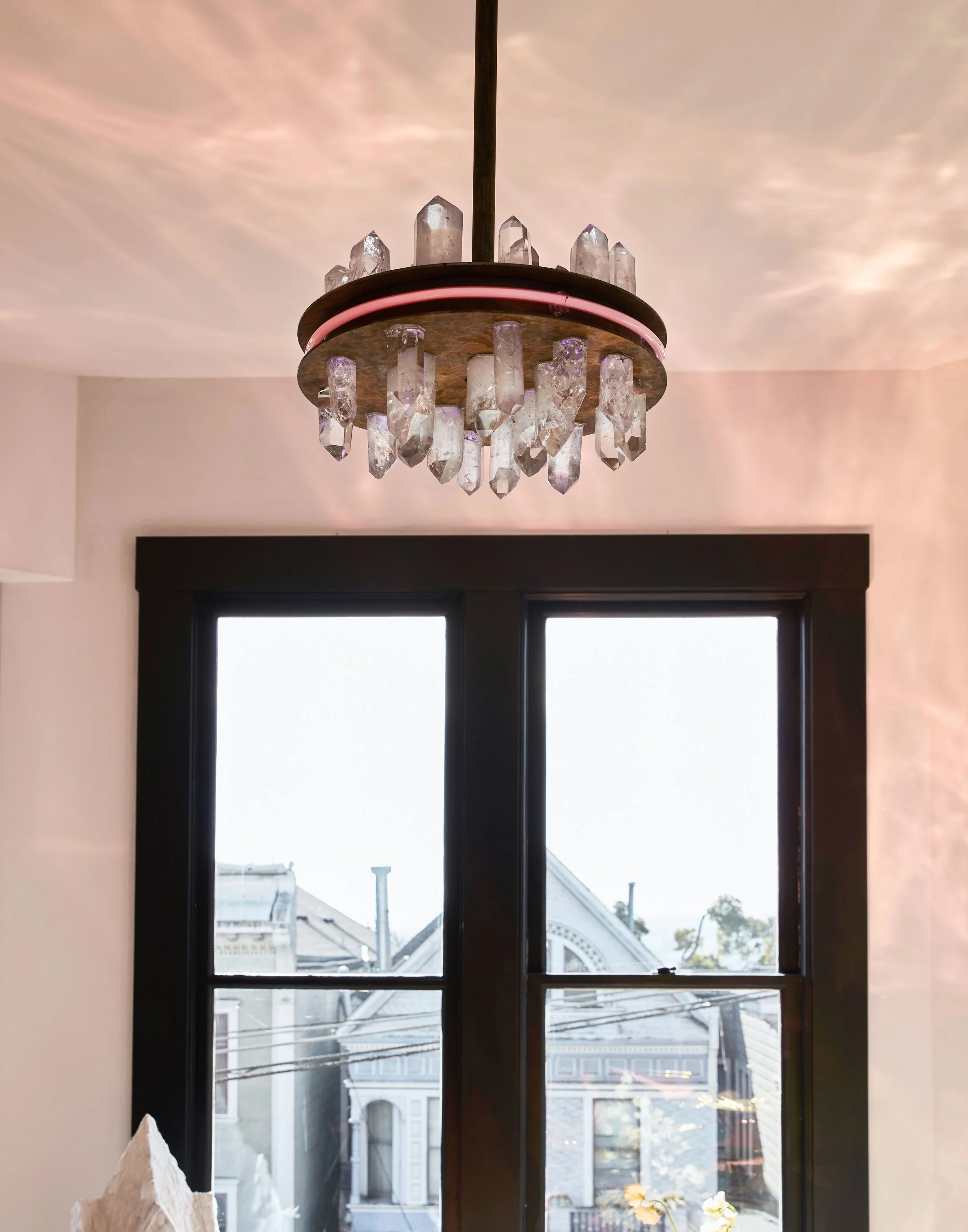 Chandelier with crystal accents hanging from a ceiling above a window showing houses outside.