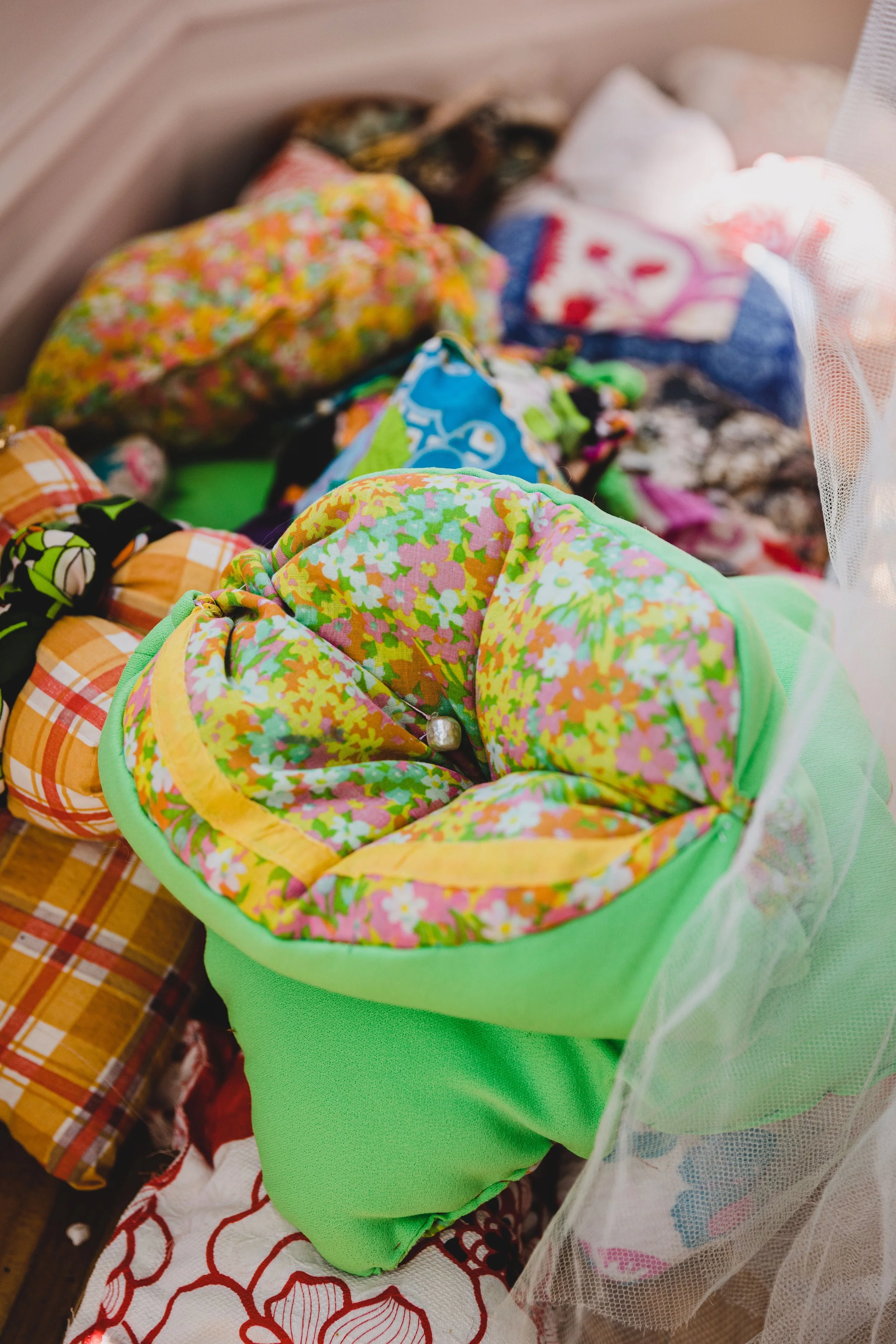 Colorful fabric and quilted items gathered together, possibly for crafting or sewing, with various patterns including floral, plaid, and abstract designs.