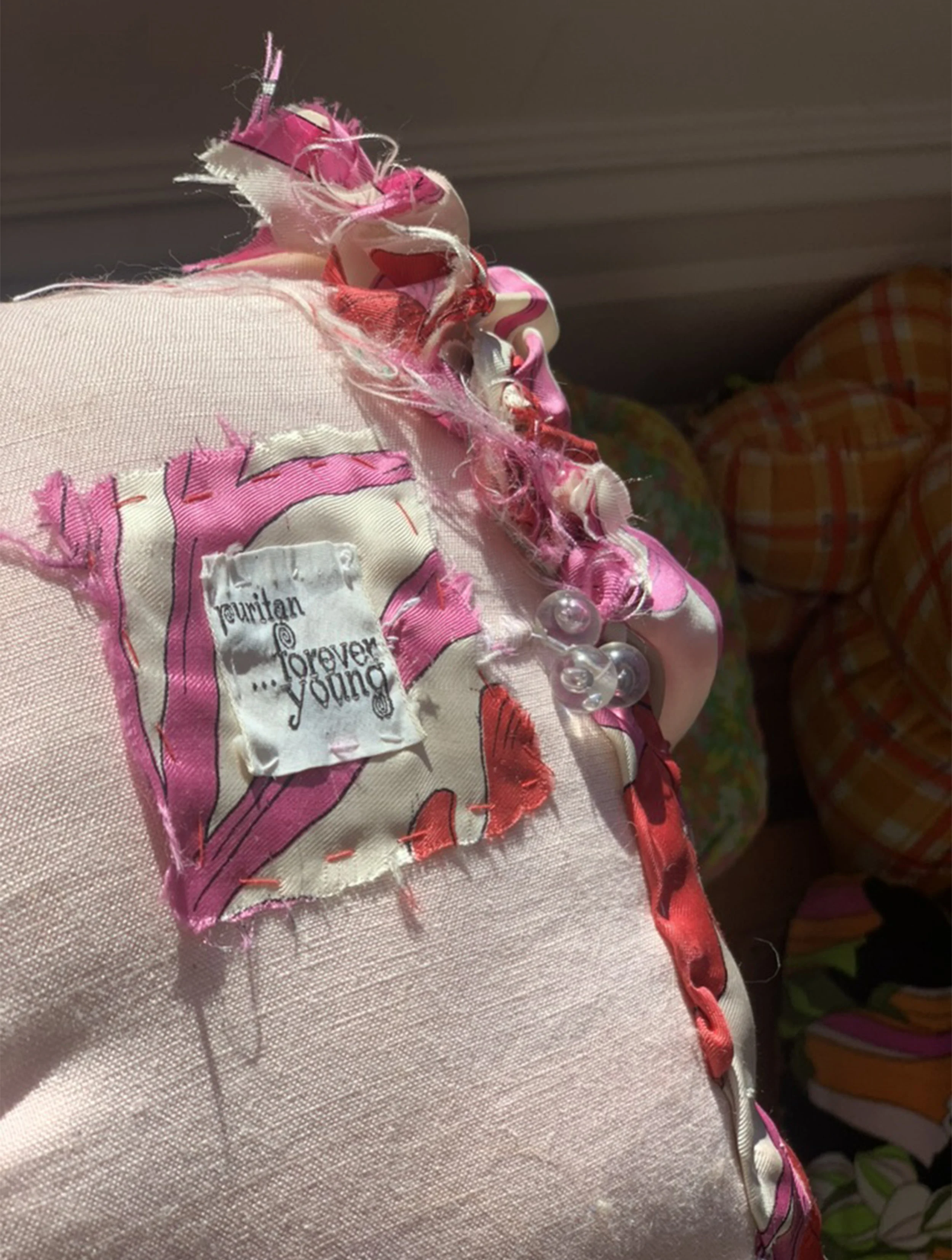 Close-up of a torn pink fabric with a clothing label reading 'fujitan ... forever young' and decorative elements like ribbons and buttons.