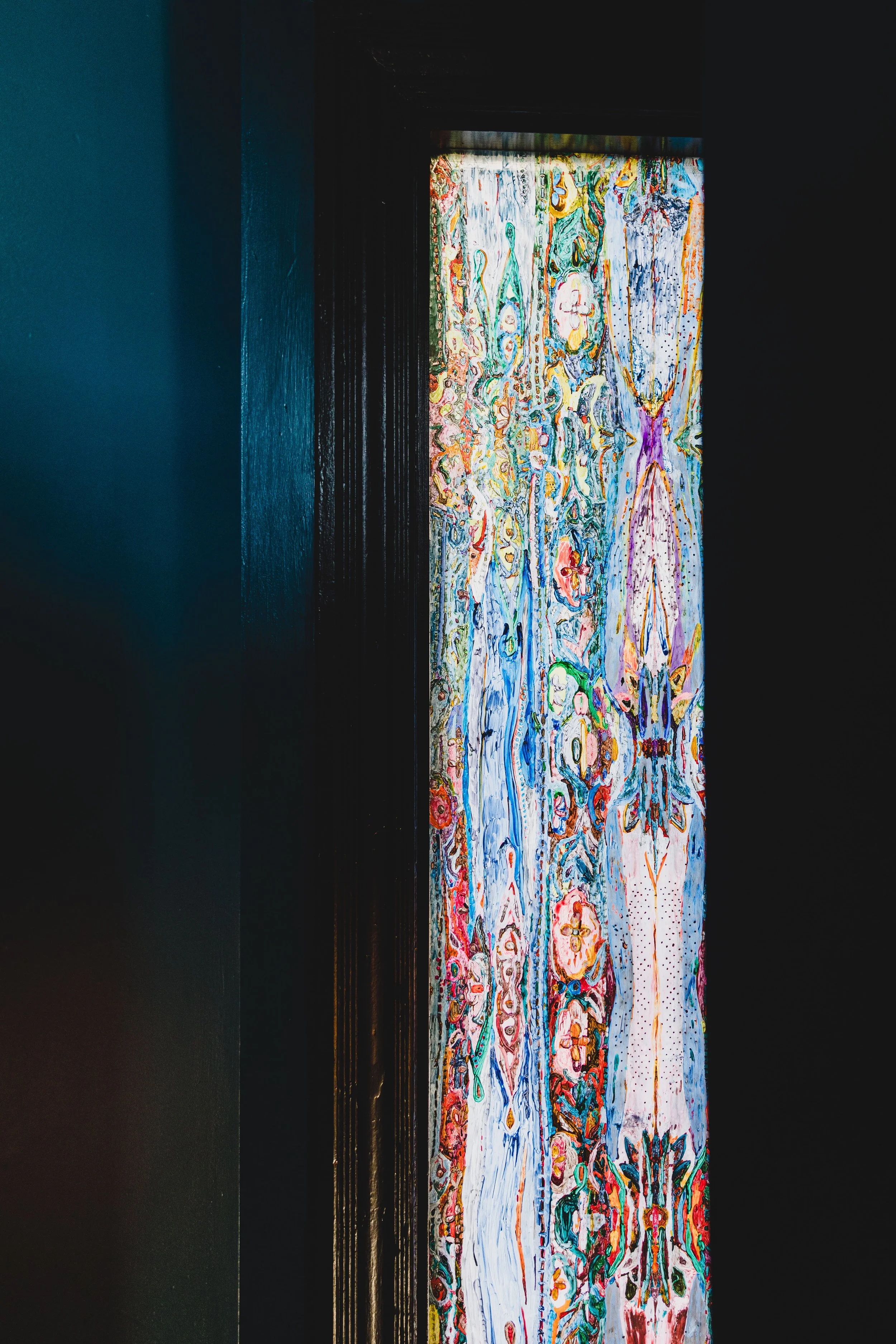 A colorful, abstract painting or fabric artwork with intricate patterns, partially seen through a dark doorway or frame.