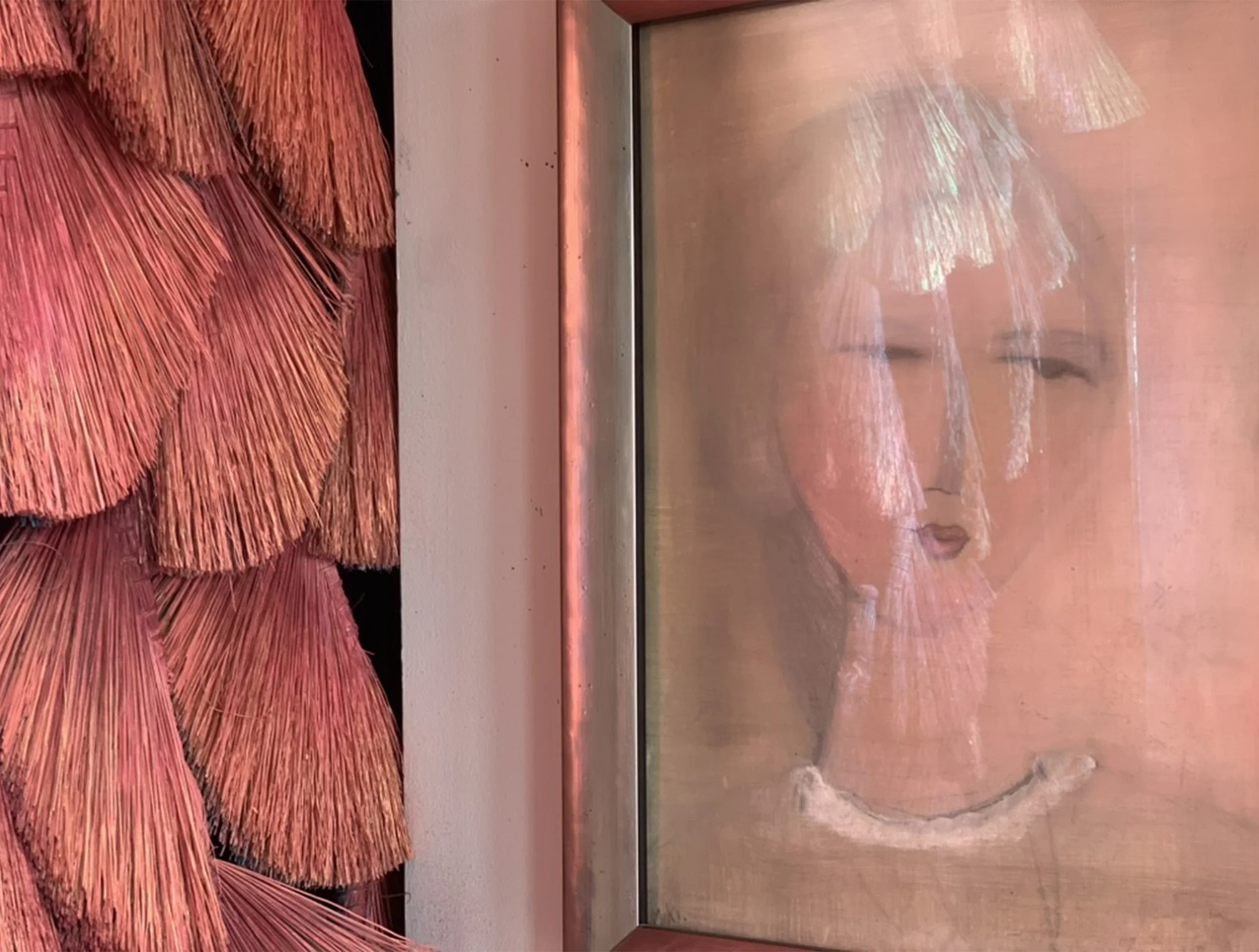 A framed artwork of a woman's face with a slightly abstract style is shown, surrounded by a textured, rust-colored, layered installation of organic or fabric elements on the left.