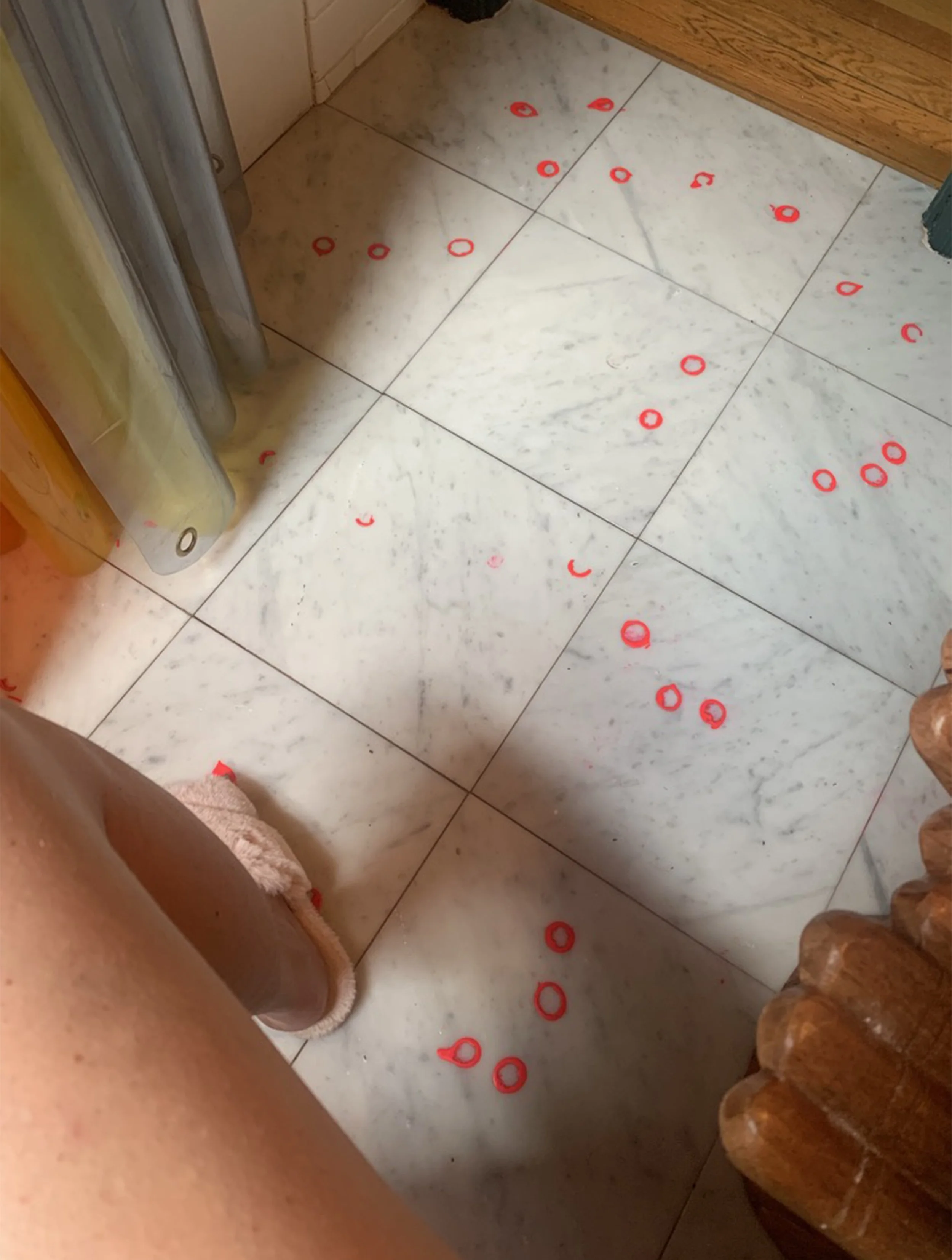 A bathroom floor with scattered red hair ties and a person's legs wearing slippers visible on the left side.