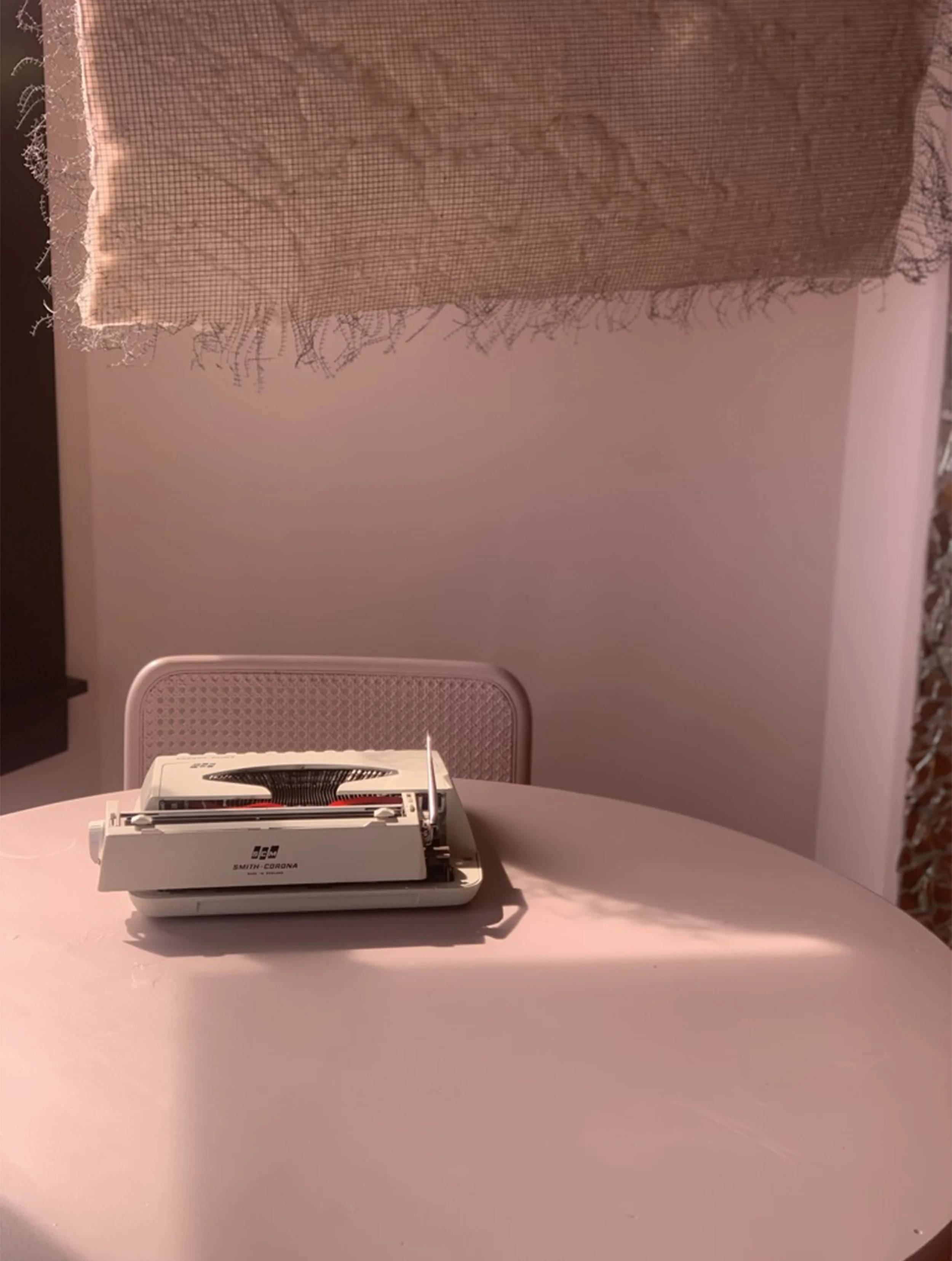 A vintage typewriter on a pink table under a hanging decorative lamp with pink and textured fabric.