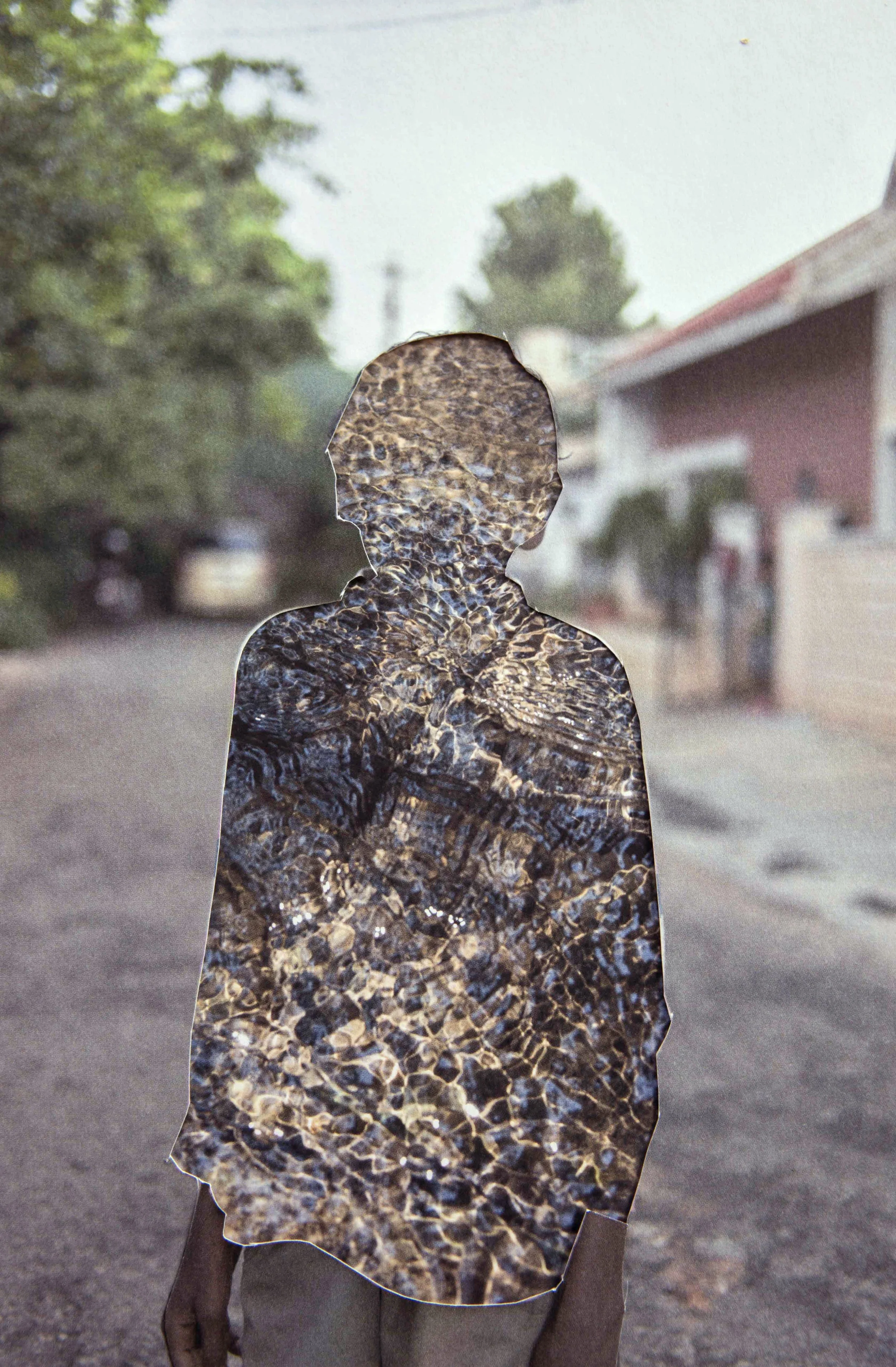 A silhouette of a person with a textured, water-reflection pattern overlay, standing on a street with trees and houses in the background.