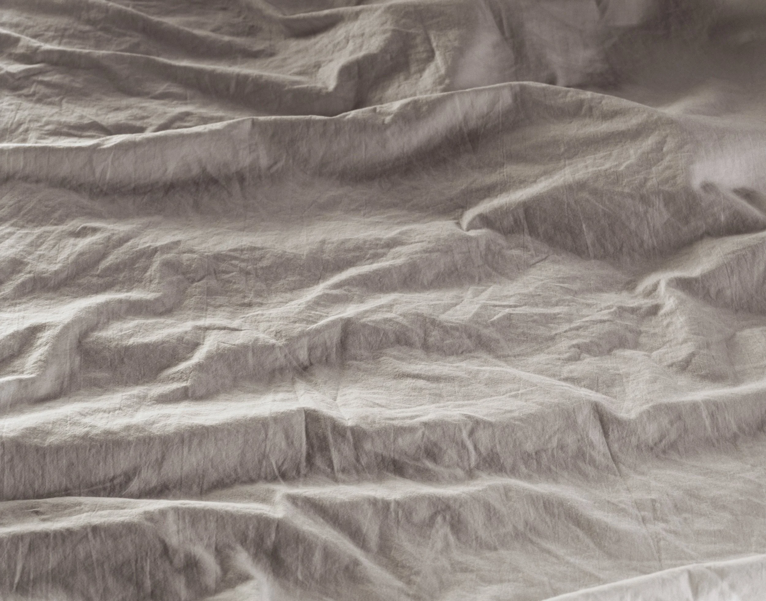 Crumpled beige or light-colored fabric or paper surface with visible wrinkles and folds.