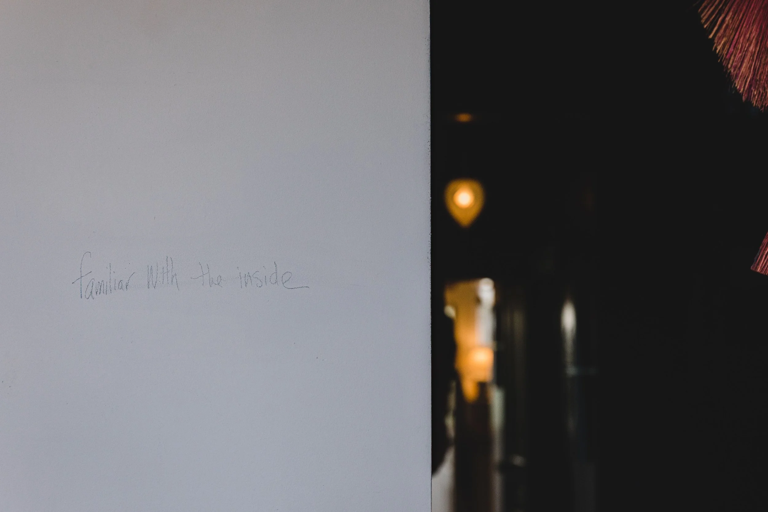 A wall with handwritten text that reads 'familiar with the inside' on the left side, contrasting with a dark interior space with warm lighting visible on the right side.