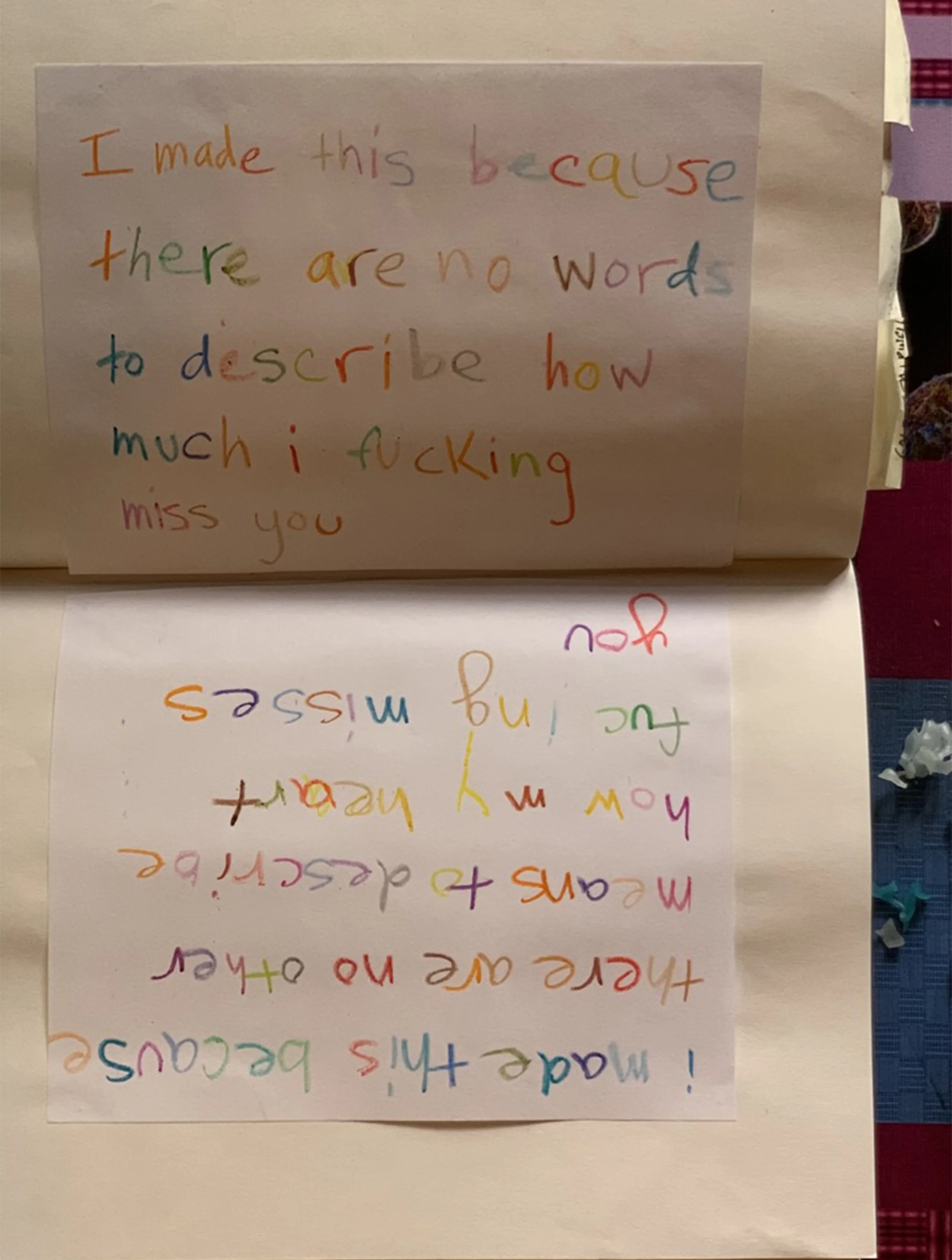 Colorful handwritten note on paper with a message expressing missing someone, with the upper note reading "I made this because there are no words to describe how much I fucking miss you" and the lower note reversed, reading "I miss you so much and I 