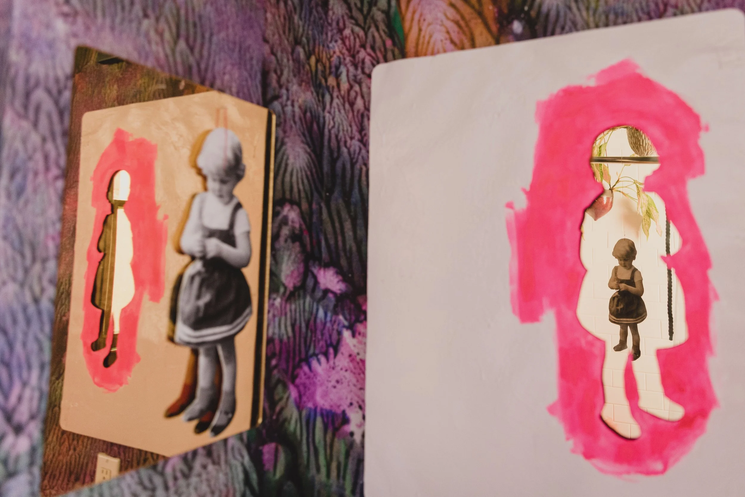 A cutout of a young girl in a dress, through which a mirror reflects her image. The cutout is painted with pink and placed inside an irregularly shaped frame.