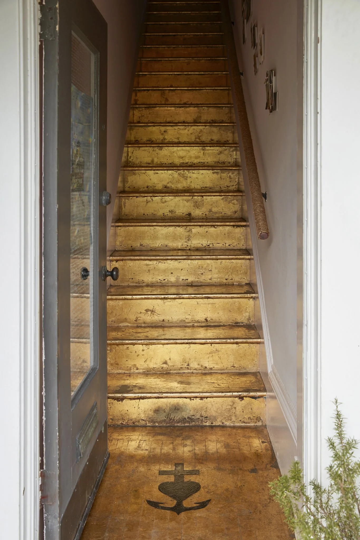 View of a wooden staircase seen from the entryway, with a nautical-themed anchor and heart symbol painted on the hardwood floor in front of the stairs.