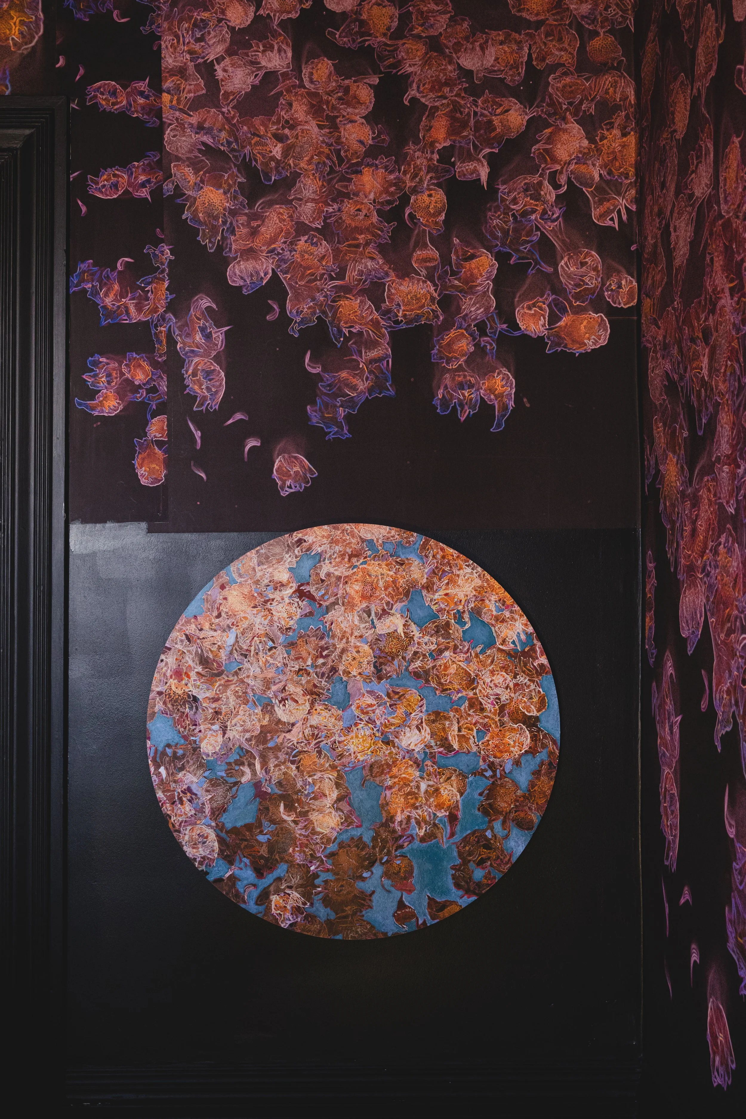 Wall with artwork of orange and purple flowers, one half-circle section filled with similar flowers, dark background, black wall trim.
