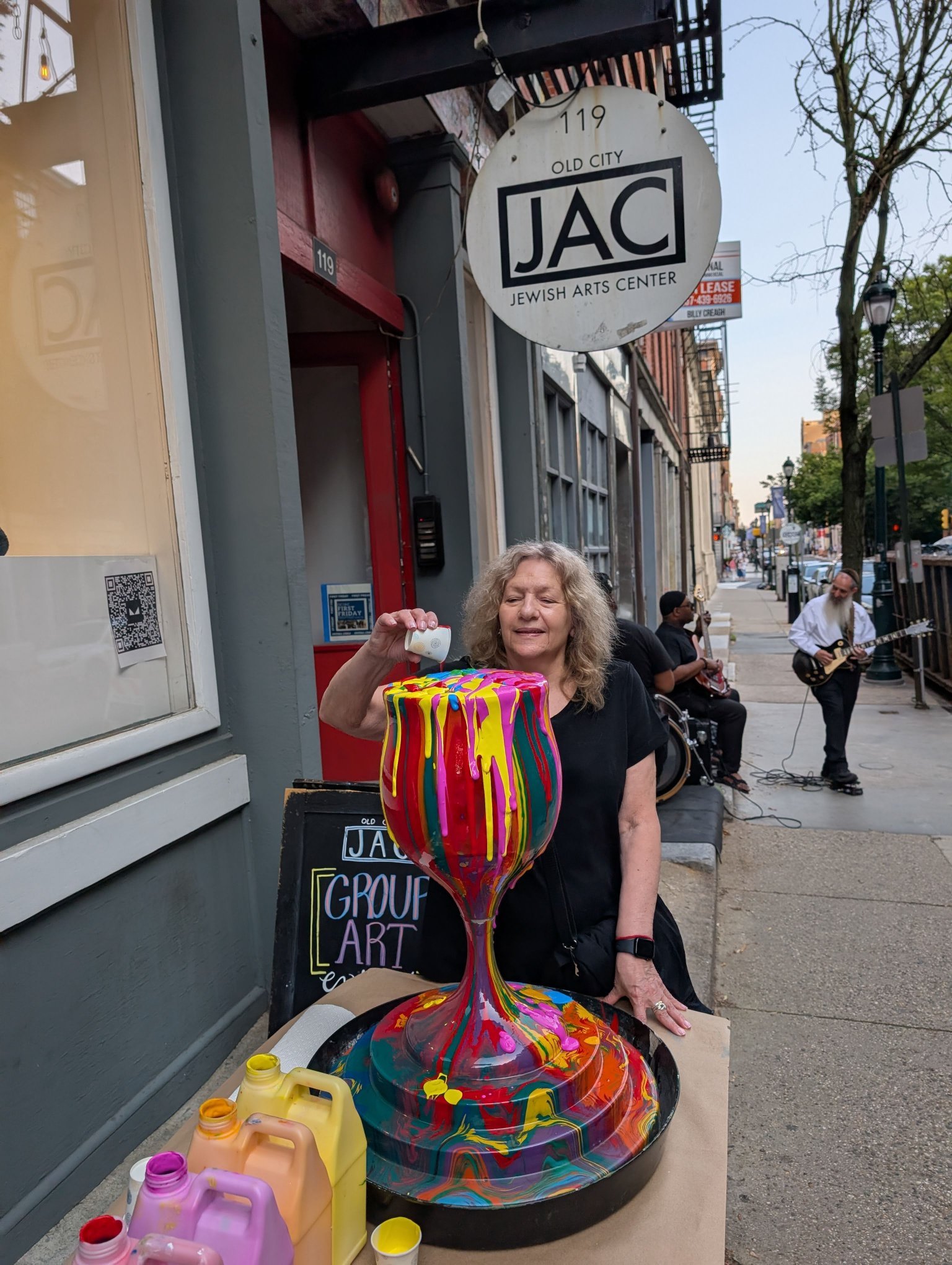 Overflowing Blessings kiddush cup sculpture at Jewish Arts Center outdoor street art event by Yitzchok Moully — colorful drip-paint Judaica installation with artist