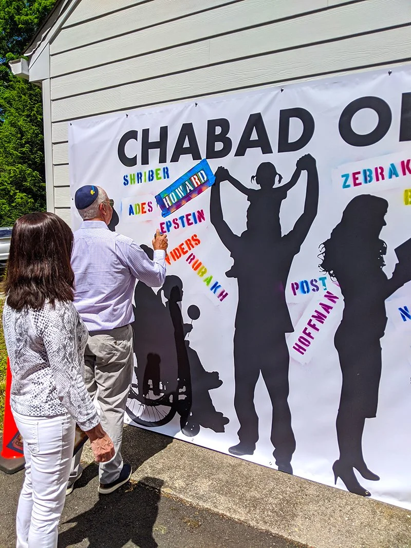 People standing outside in front of a large banner with colorful text and silhouettes, including a woman in a wheelchair and a child sitting on an adult's shoulders.