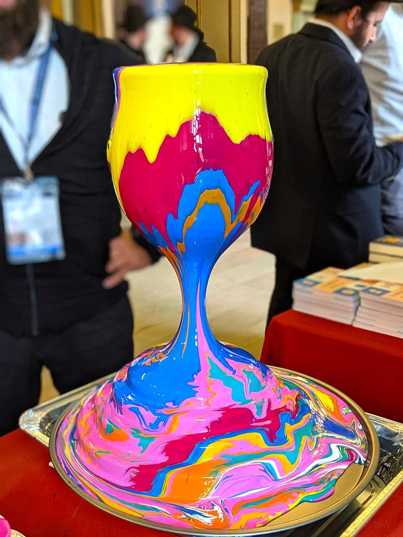 A colorful, swirl-painted goblet on a tray with a vibrant mix of yellow, pink, blue, and orange colors.