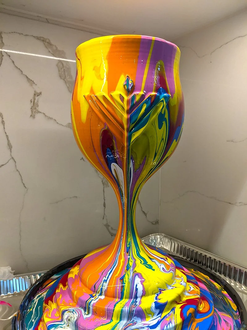 A colorful, abstract sculpture resembling a goblet with swirling patterns of yellow, orange, purple, green, blue, and white paint.