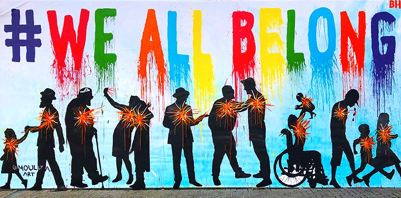 Colorful mural with hashtag #WEALLBELONG and silhouettes of diverse people holding hands and children, symbolizing unity and inclusion.