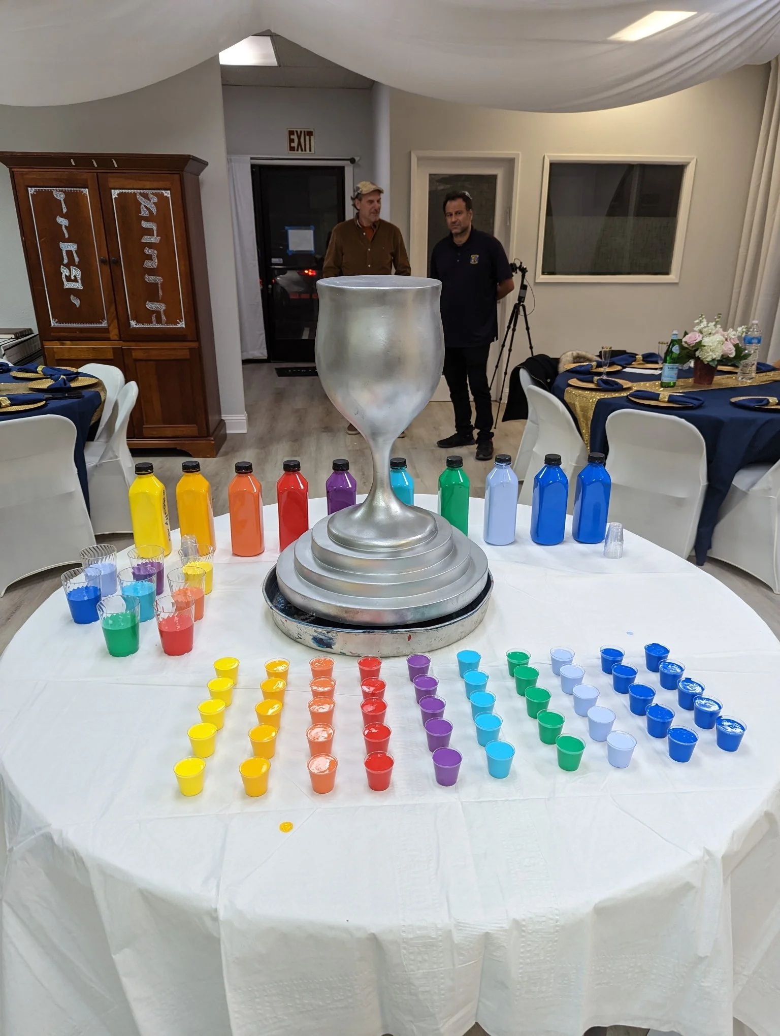 Overflowing Blessings activity setup by Yitzchok Moully at Jewish celebration — colorful paint cups in rainbow order at bar mitzvah or gala event