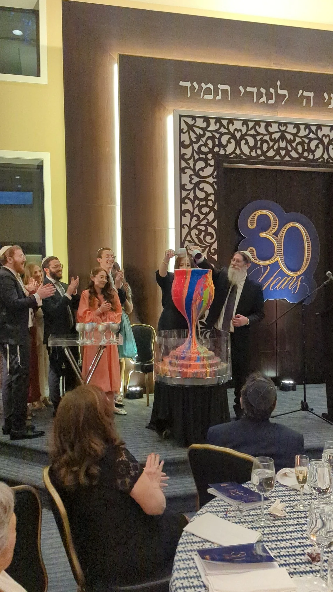 30th anniversary Jewish gala celebration featuring Yitzchok Moully art — guests clapping at formal dinner with Overflowing Blessings display