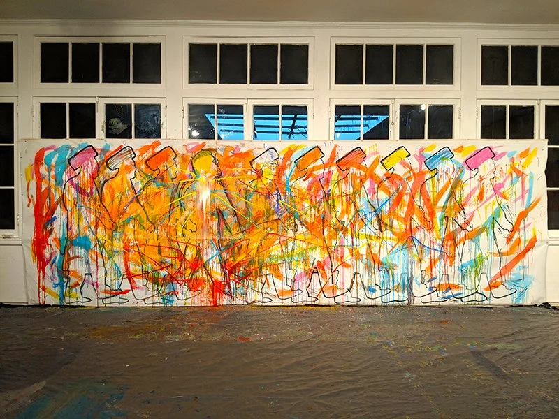 Large abstract mural with colorful splashes of orange, yellow, blue, pink, green, and purple paint, featuring black outline silhouettes of people, on a white wall in an indoor setting.