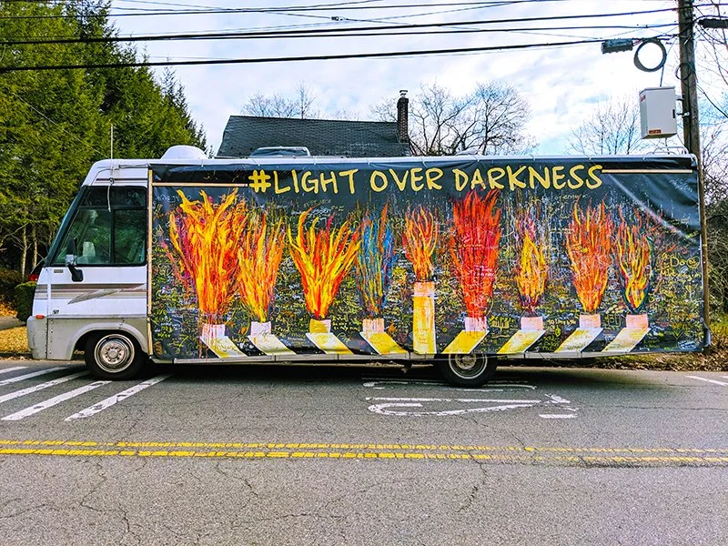 A school bus painted with colorful flames and the hashtag #LIGHT OVER DARKNESS.
