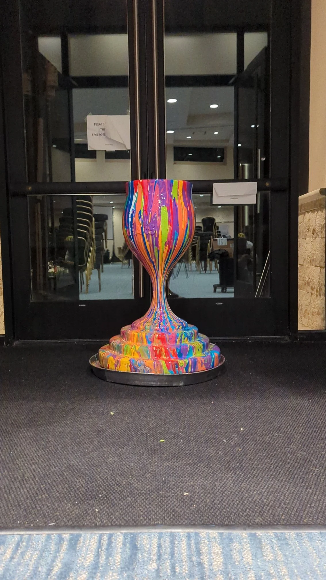 Overflowing Blessings kiddush cup sculpture by Yitzchok Moully — colorful drip-paint wine glass Jewish art displayed at indoor event venue