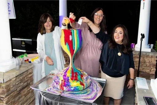 Women participating in Yitzchok Moully’s interactive Overflowing Blessings art activity — colorful rainbow paint pour at outdoor Jewish community event