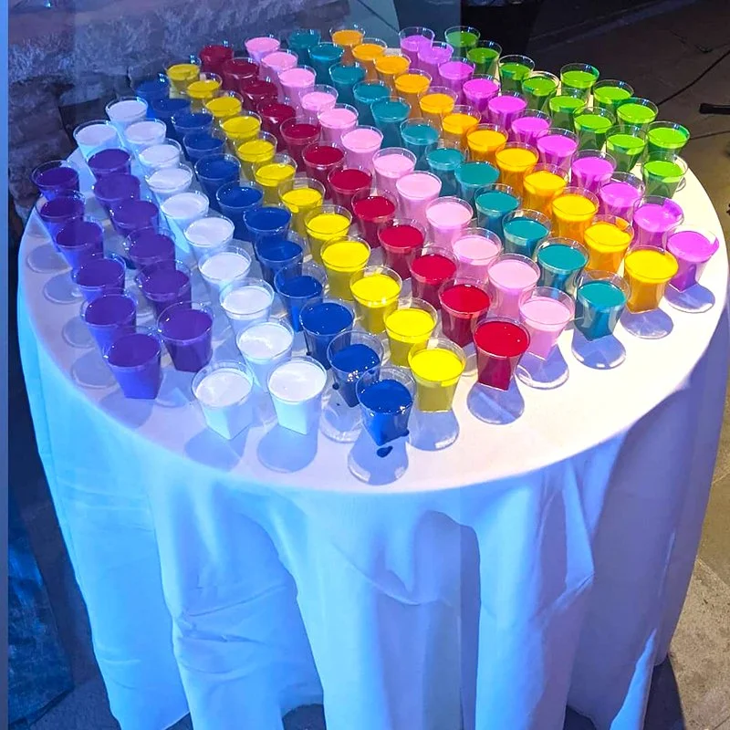 Colorful shot glasses arranged in rows on a round table covered with a white tablecloth.