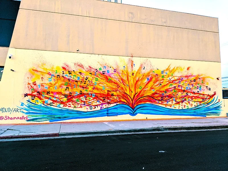 Colorful mural of an open book with pages turning into vibrant flames and musical notes, painted on a wall.