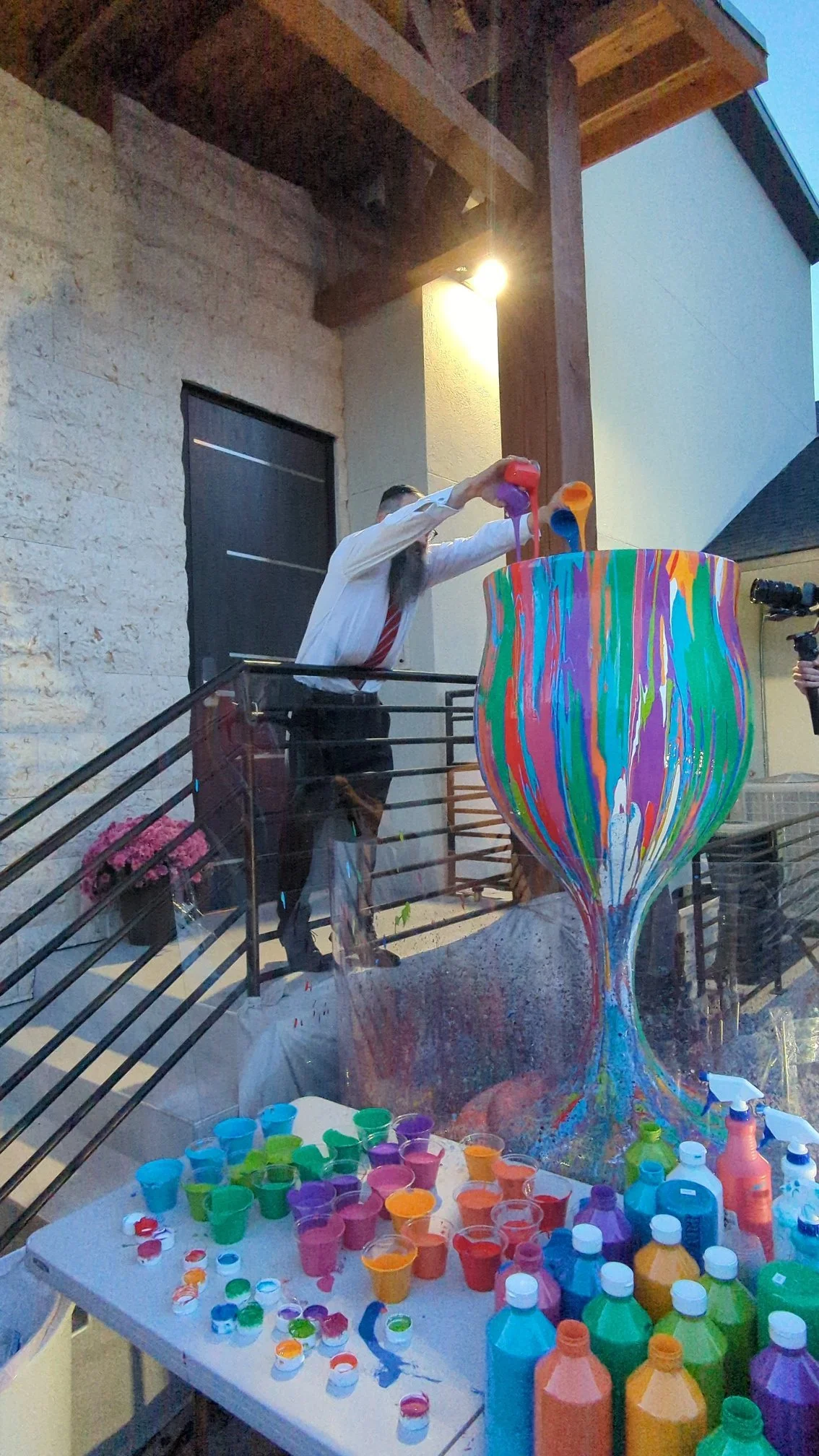 Man pouring paint into Overflowing Blessings vase at nighttime outdoor event by Yitzchok Moully — interactive Jewish art activity, stone wall venue