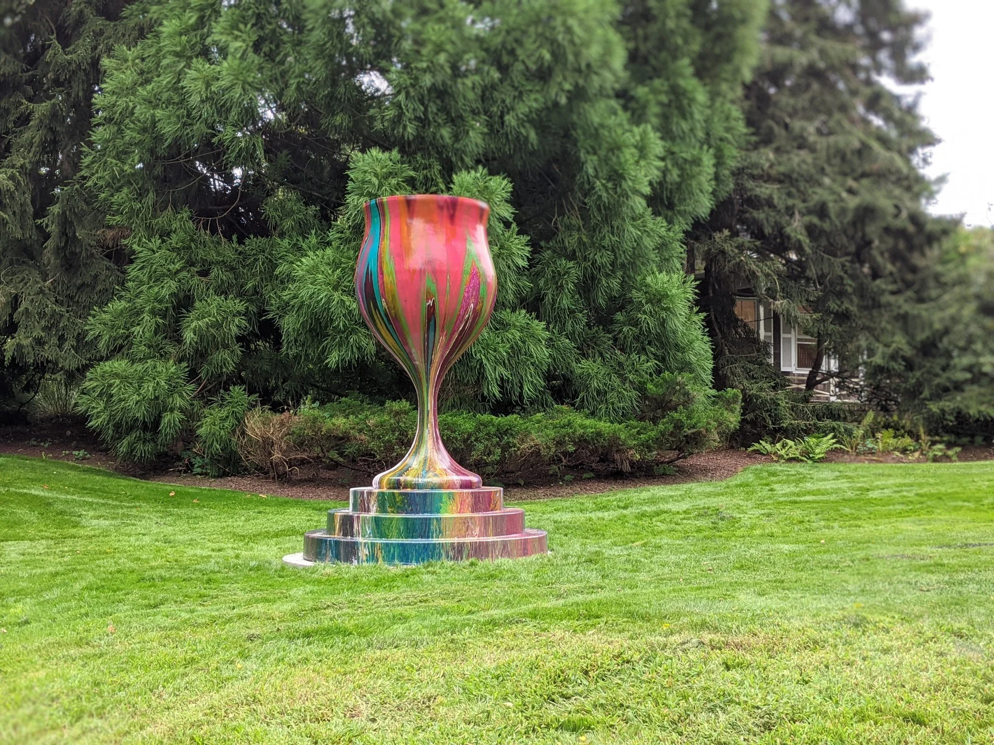 Overflowing Blessings kiddush cup sculpture by Yitzchok Moully — colorful red Jewish art installation on tiered base in lush garden setting