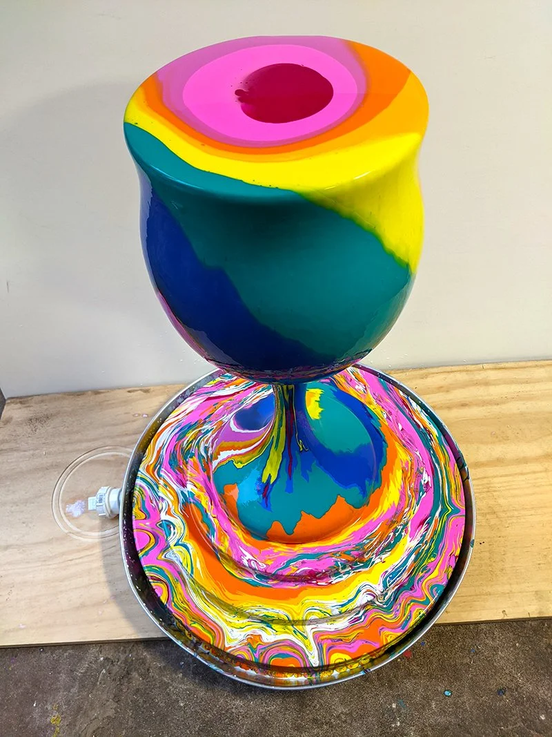 A colorful spin art machine creating vibrant, swirling patterns with bright pink, yellow, green, blue, and orange colors on a wooden and metal surface.