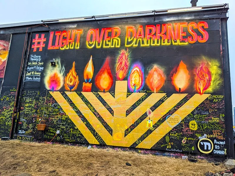 Colorful mural depicting multiple lit menorah candles and the hashtag #LightOverDarkness at the top.