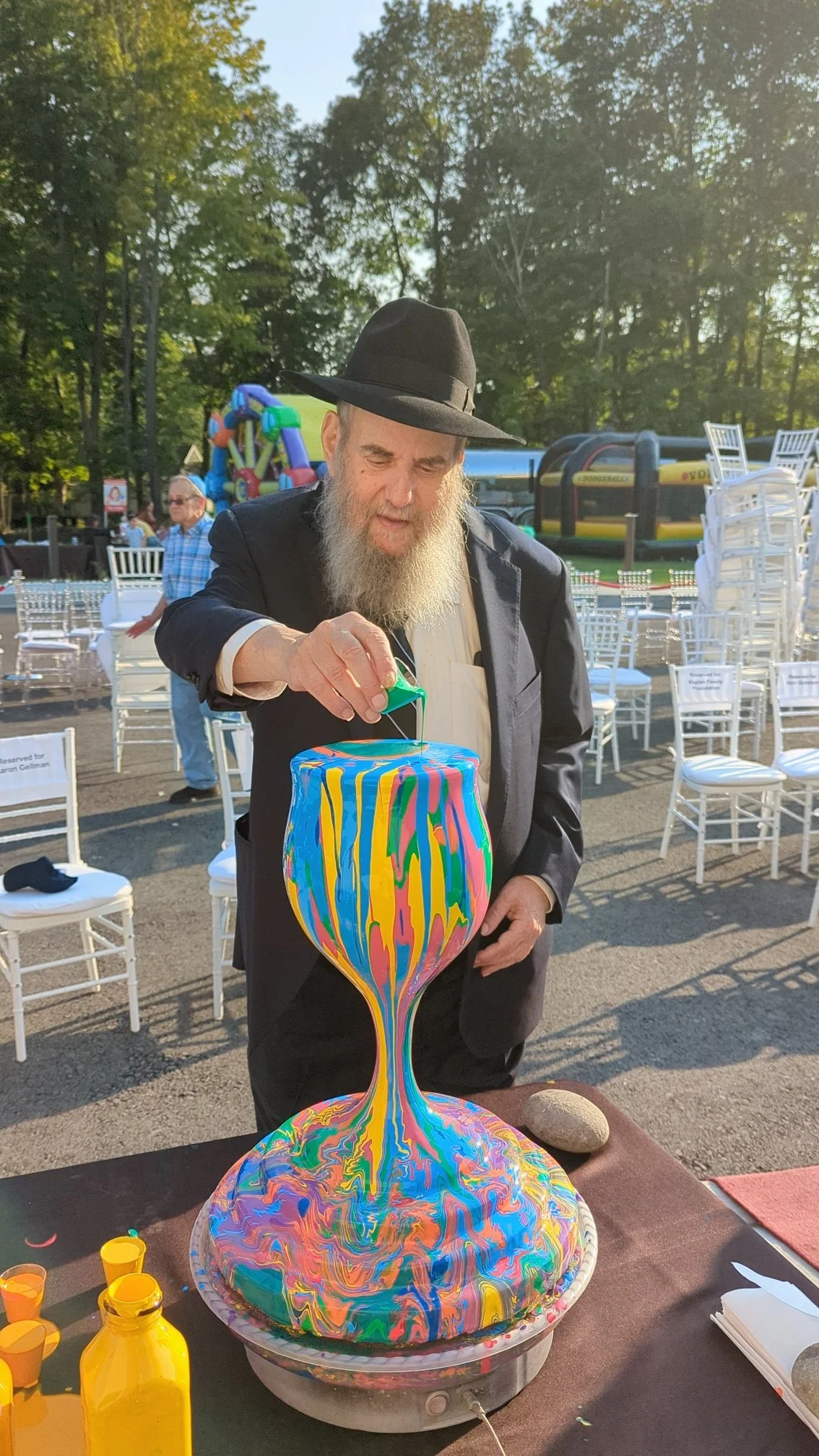 Yitzchok Moully creating Overflowing Blessings kiddush cup sculpture at outdoor Jewish community art event — artist in traditional black hat and suit