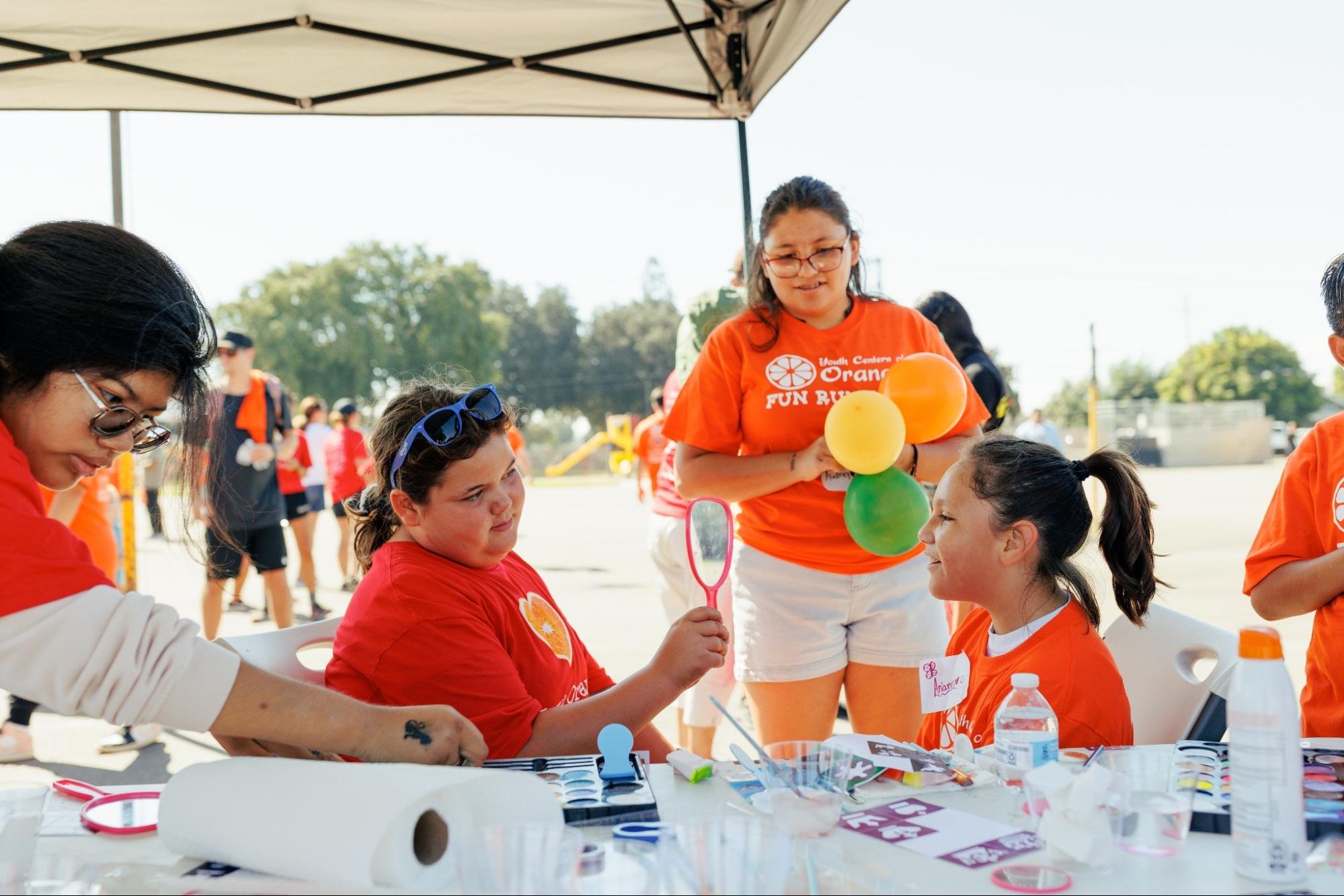    A face painter shows her design by holding up a mirror to the girl who received the face paint at the Youth Centers of Orange Fun Run on Oct. 7, 2023.   