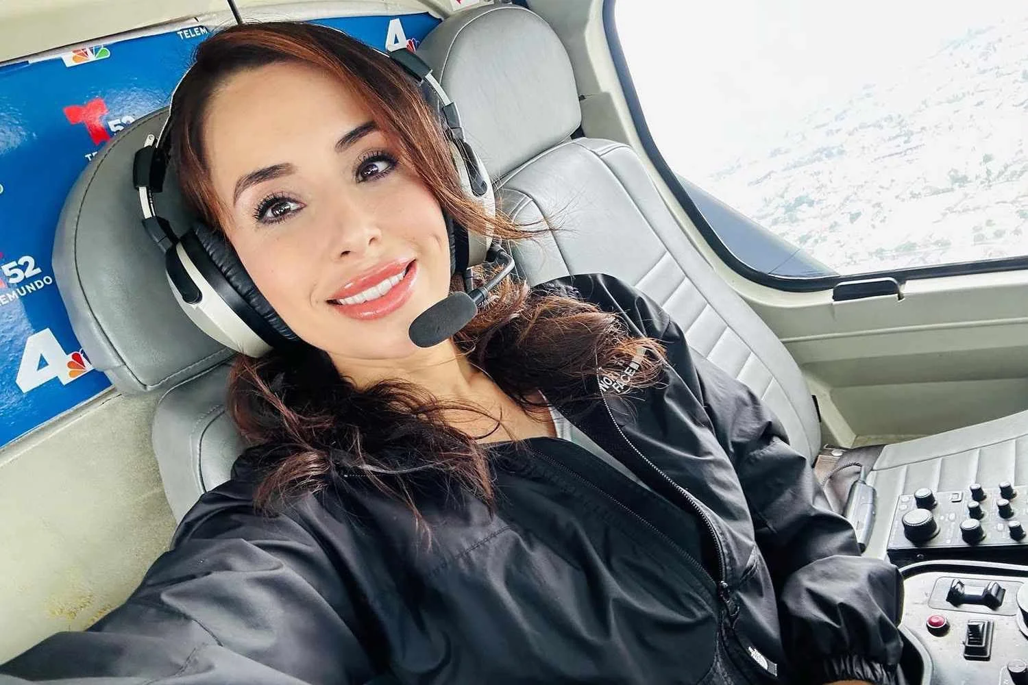 Selfie of Eliana Moreno in a helicopter wearing a headset and black jacket smiling.