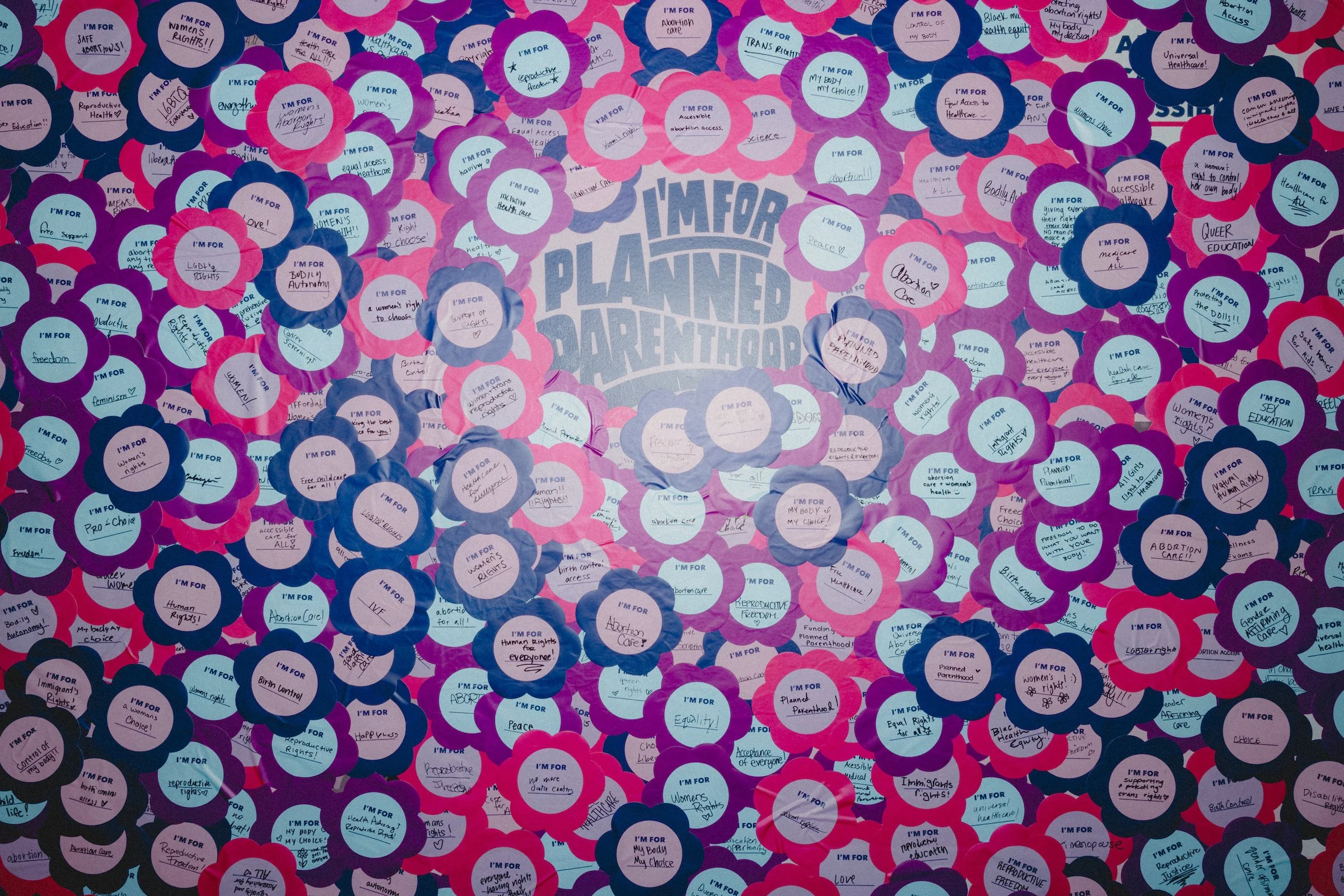 A flower-covered 'I'm for Planned Parenthood' wall filled with handwritten messages supporting reproductive rights at Daisy Chain Fields Music Festival.
